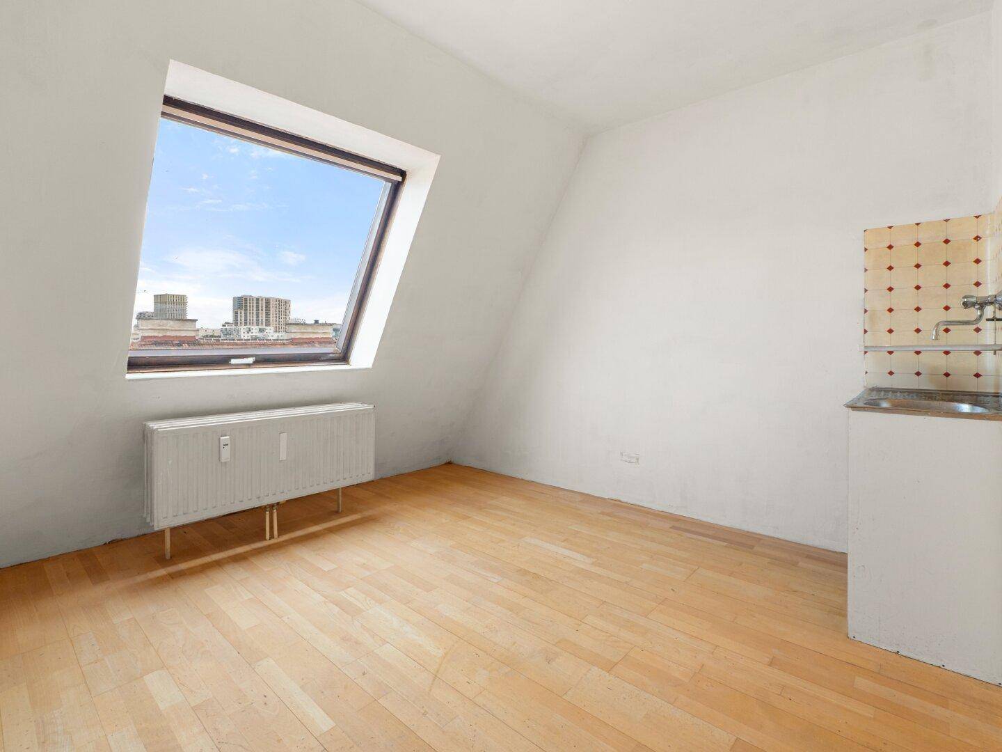 Heller Raum mit Holzfußboden, Dachfenster und einem kleinen Waschbeckenbereich.