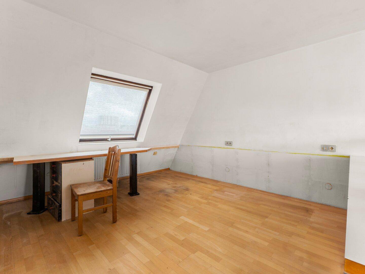 Helles Arbeitszimmer mit Holzfußboden, Dachfenster und integriertem Schreibtisch unter der Schräge.