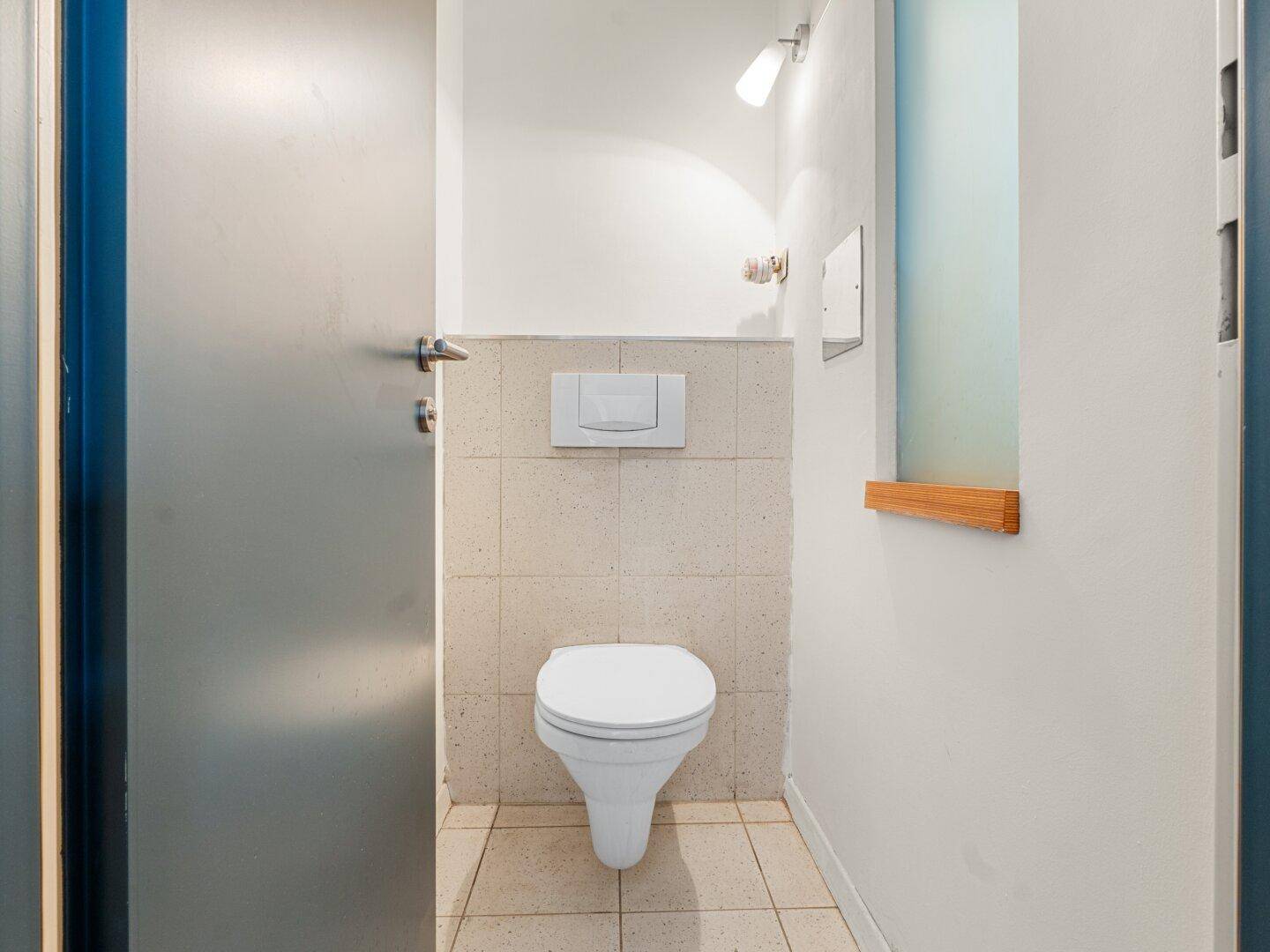Kompaktes Gäste-WC mit wandhängender Toilette und hellen Fliesen.