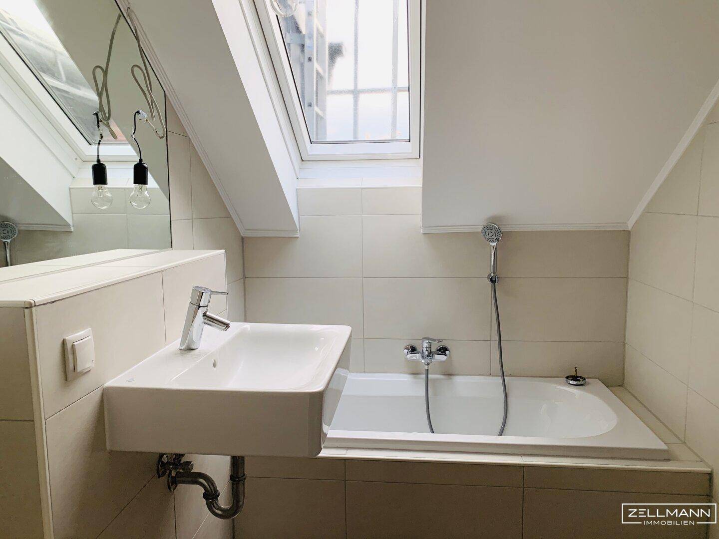 Modernes Badezimmer im Dachgeschoss mit Badewanne, Waschbecken und einem Dachfenster für natürliches Licht.