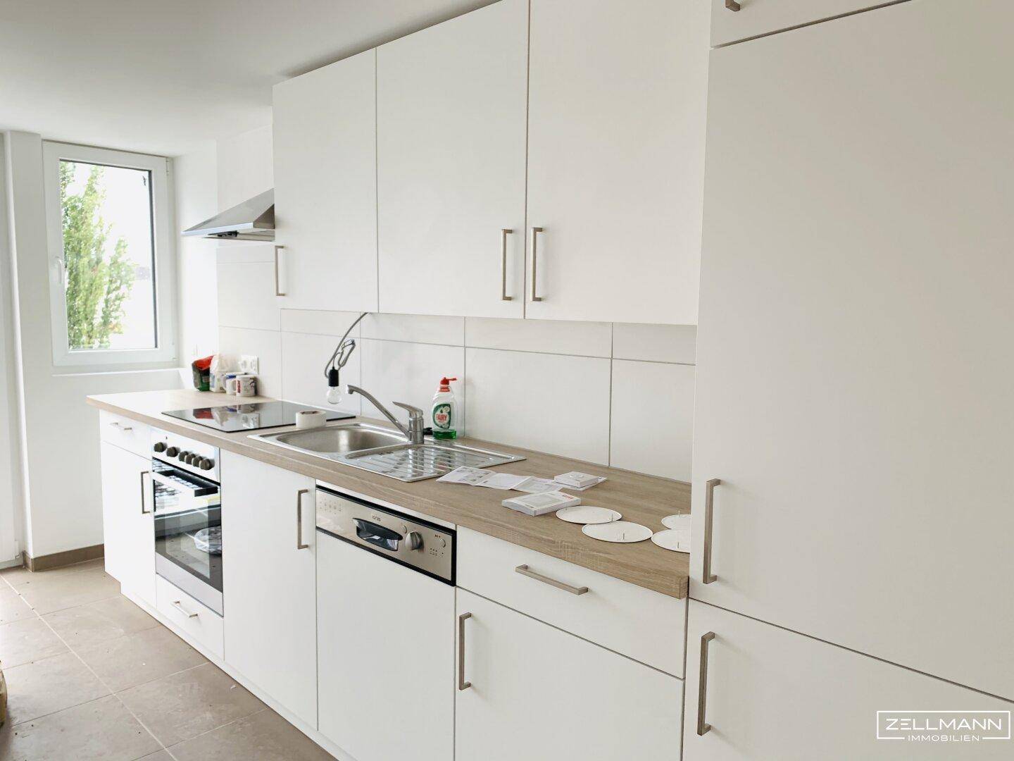 Funktionale weiße Einbauküche mit Holz-Arbeitsplatte, Spüle, Herd und Geschirrspüler, neben einem Fenster.