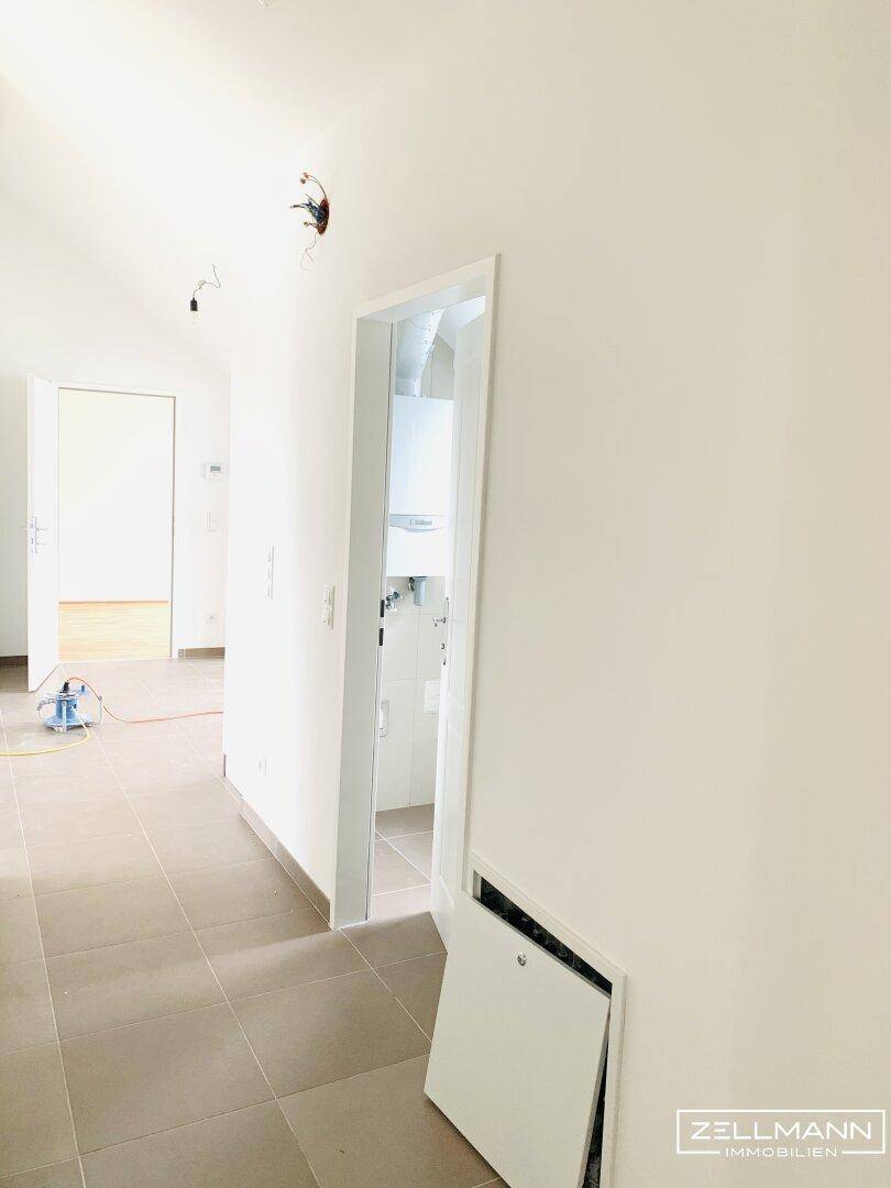 Heller Flur mit Fliesenboden und Zugang zu einem Raum mit Heizungsanlage, noch im Bauzustand.