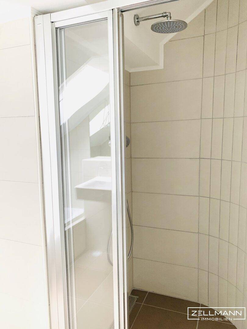 Moderne Duschkabine mit Glasabtrennung und Regendusche in einem gefliesten Badezimmer im Dachgeschoss.