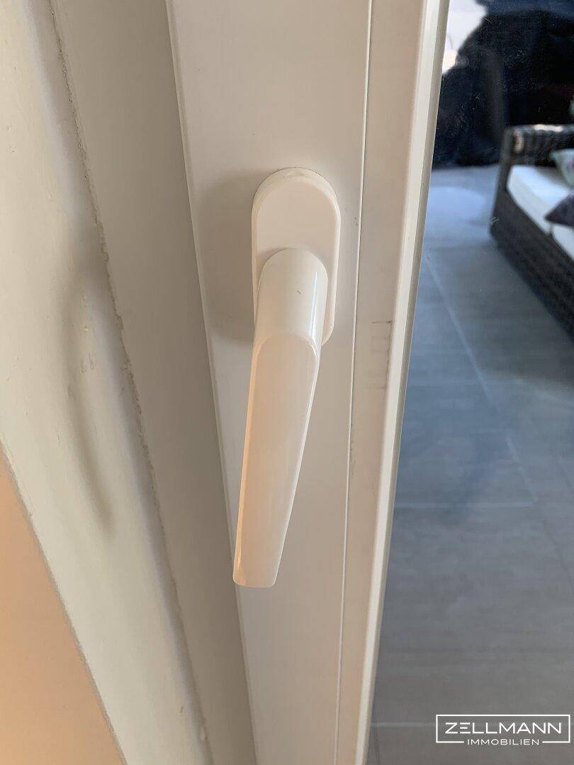 Nahaufnahme eines weißen Fenstergriffs an einem modernen Fensterrahmen.