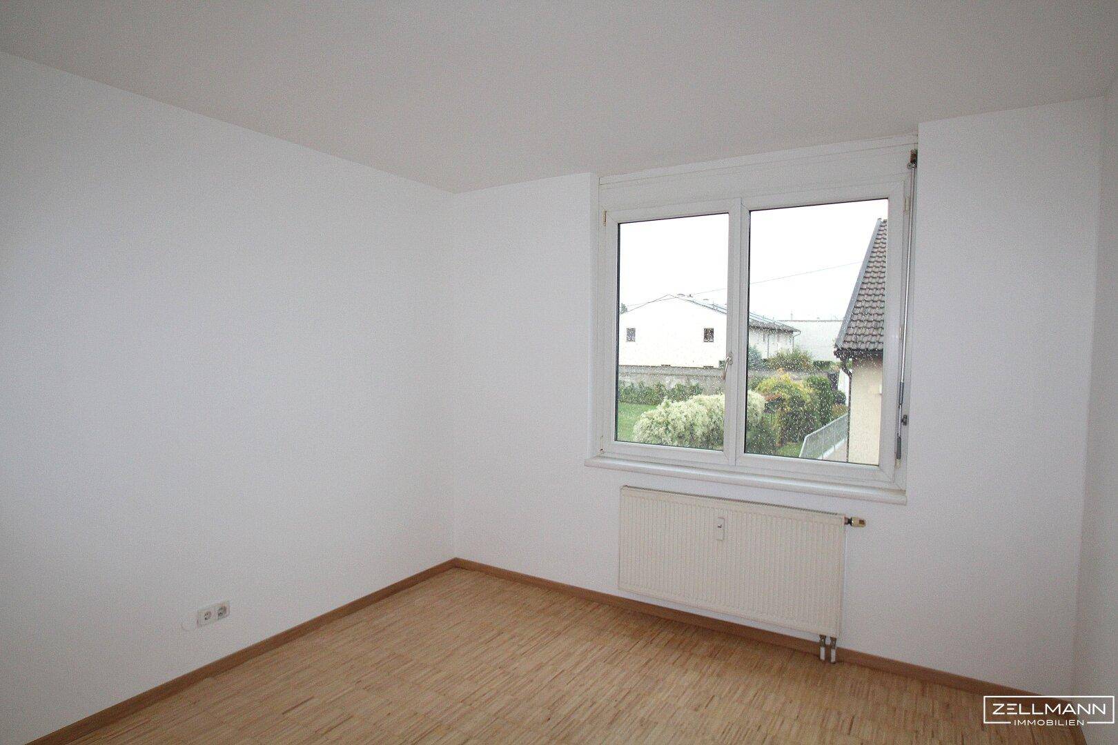 Helles Zimmer mit Parkettboden und großem Fenster, das einen angenehmen Blick ins Grüne bietet.