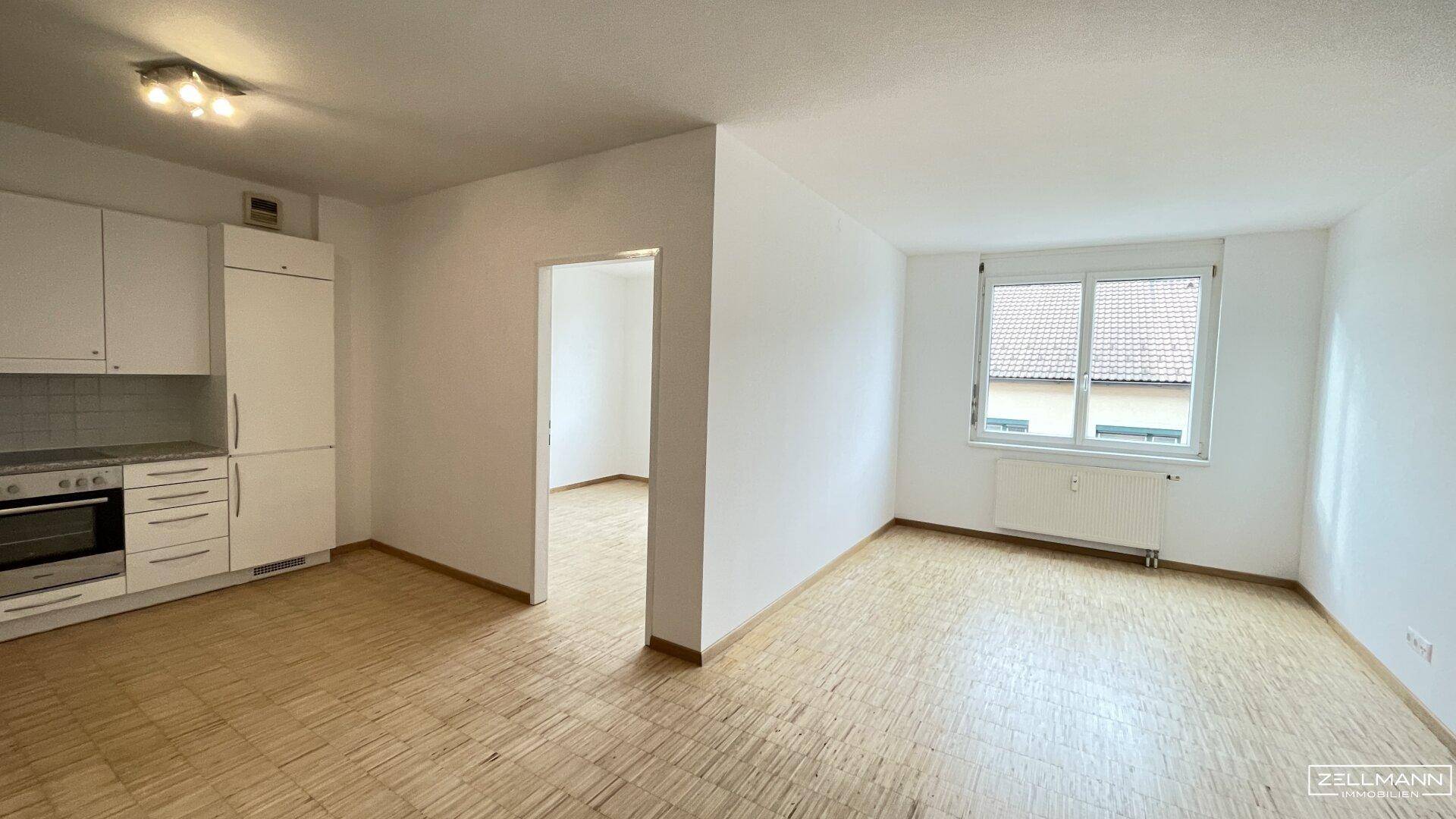 Geräumiger Wohn- und Essbereich mit offener Küche, Parkettboden und viel Tageslicht durch das Fenster.
