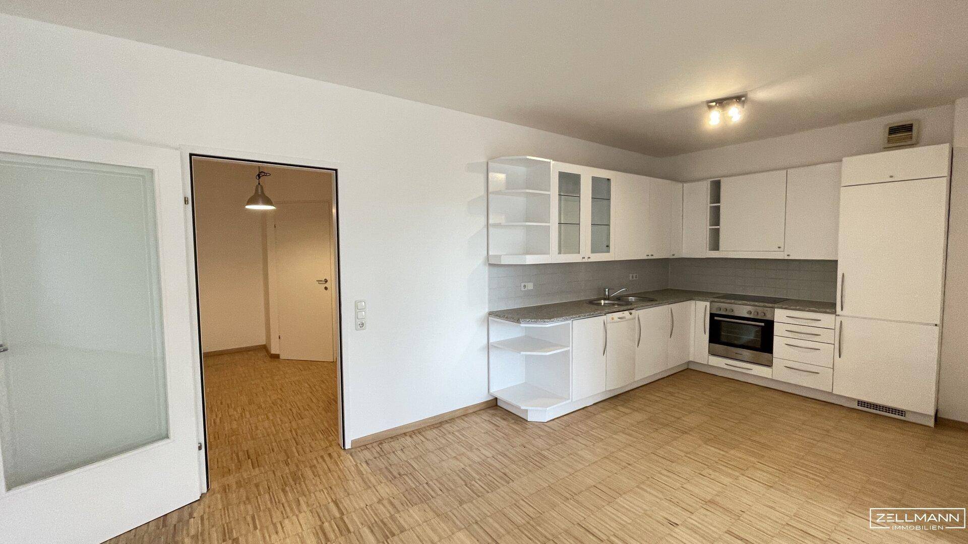 Moderne Einbauküche mit weißen Fronten und direktem Zugang zu einem angrenzenden Wohnbereich.