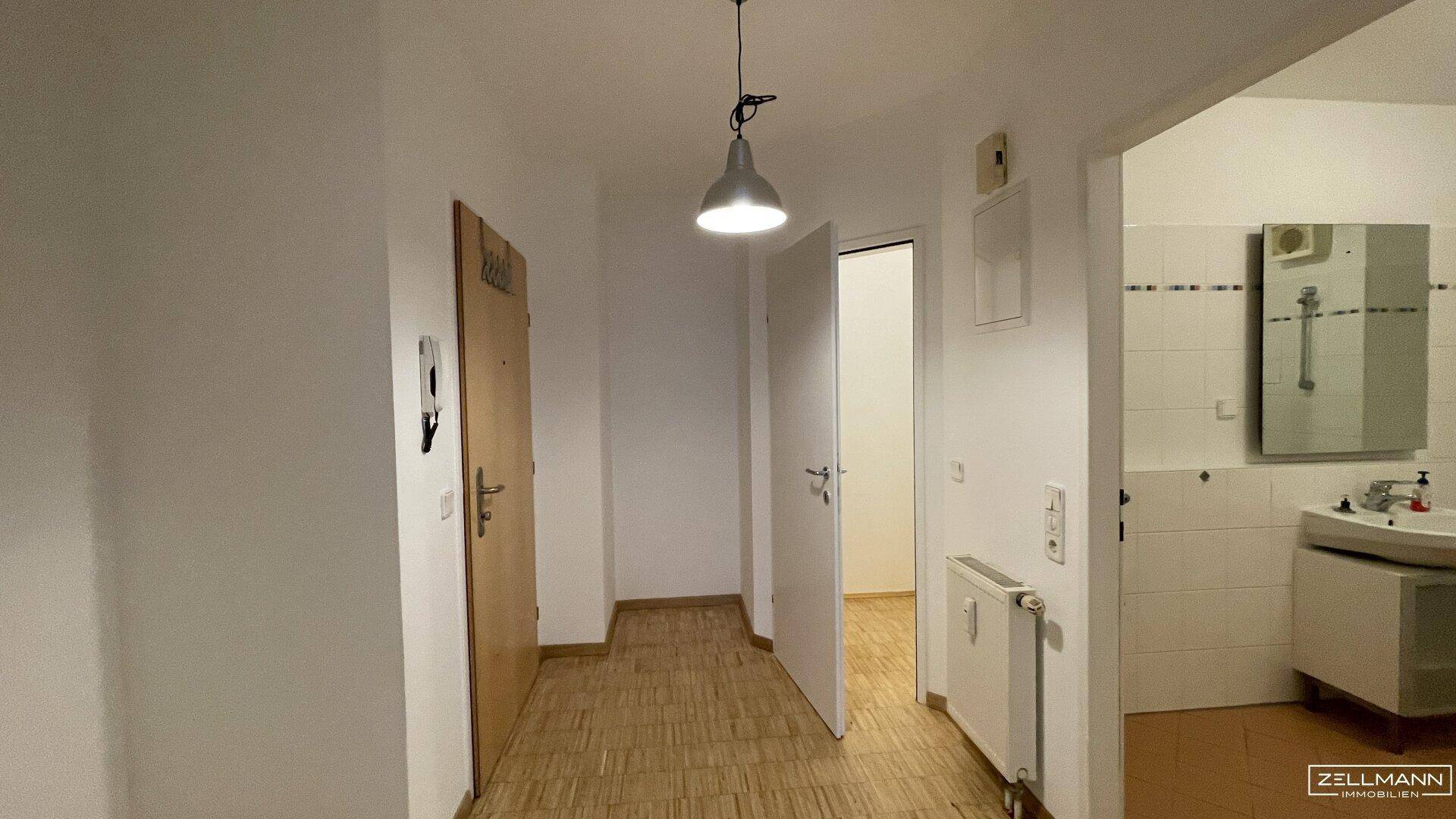 Heller Flur mit Parkettboden, Zugang zu verschiedenen Räumen und einem Blick ins Badezimmer.
