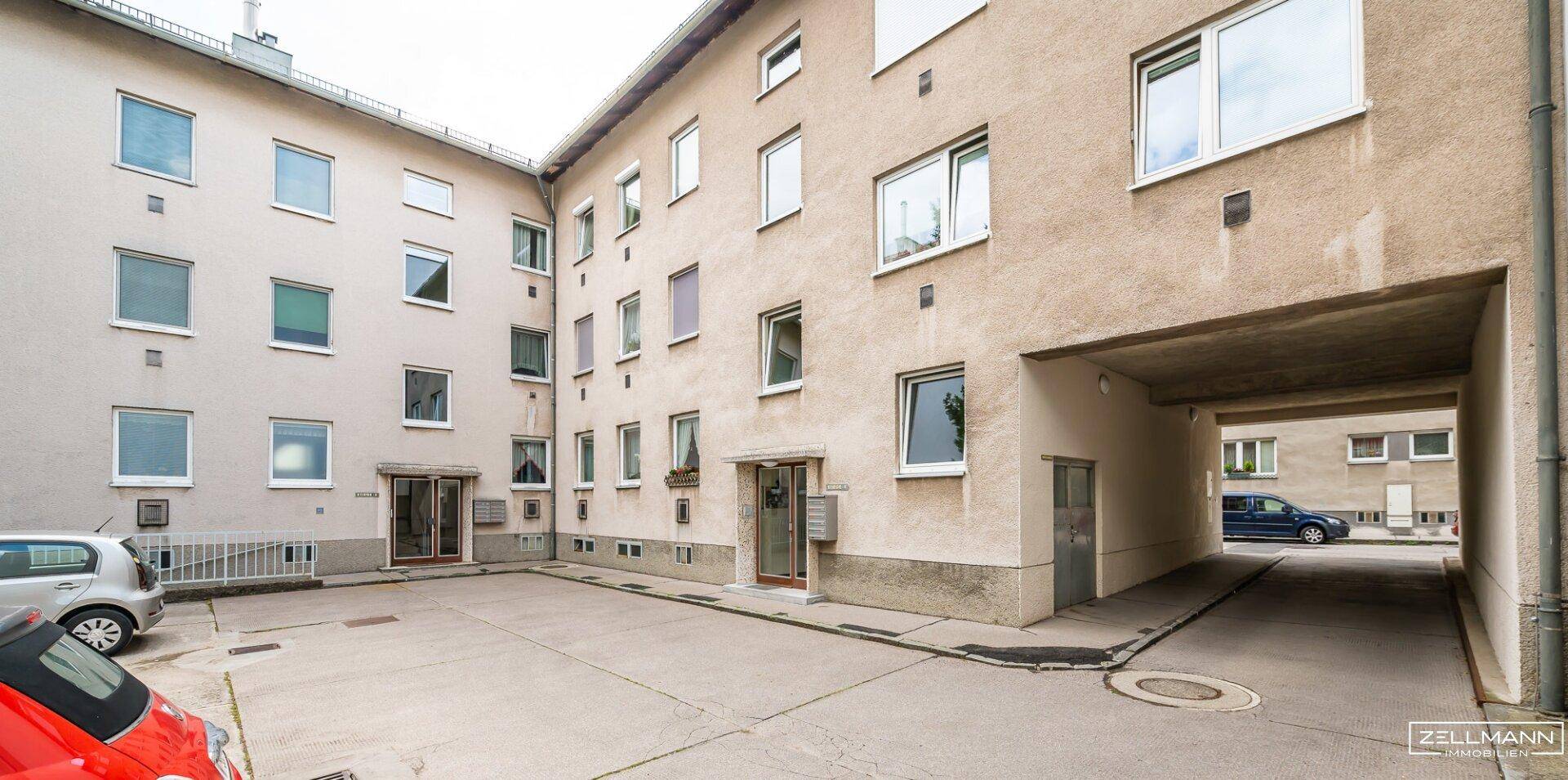 Innenhof eines Mehrfamilienhauses mit Durchfahrt und geparkten Fahrzeugen.