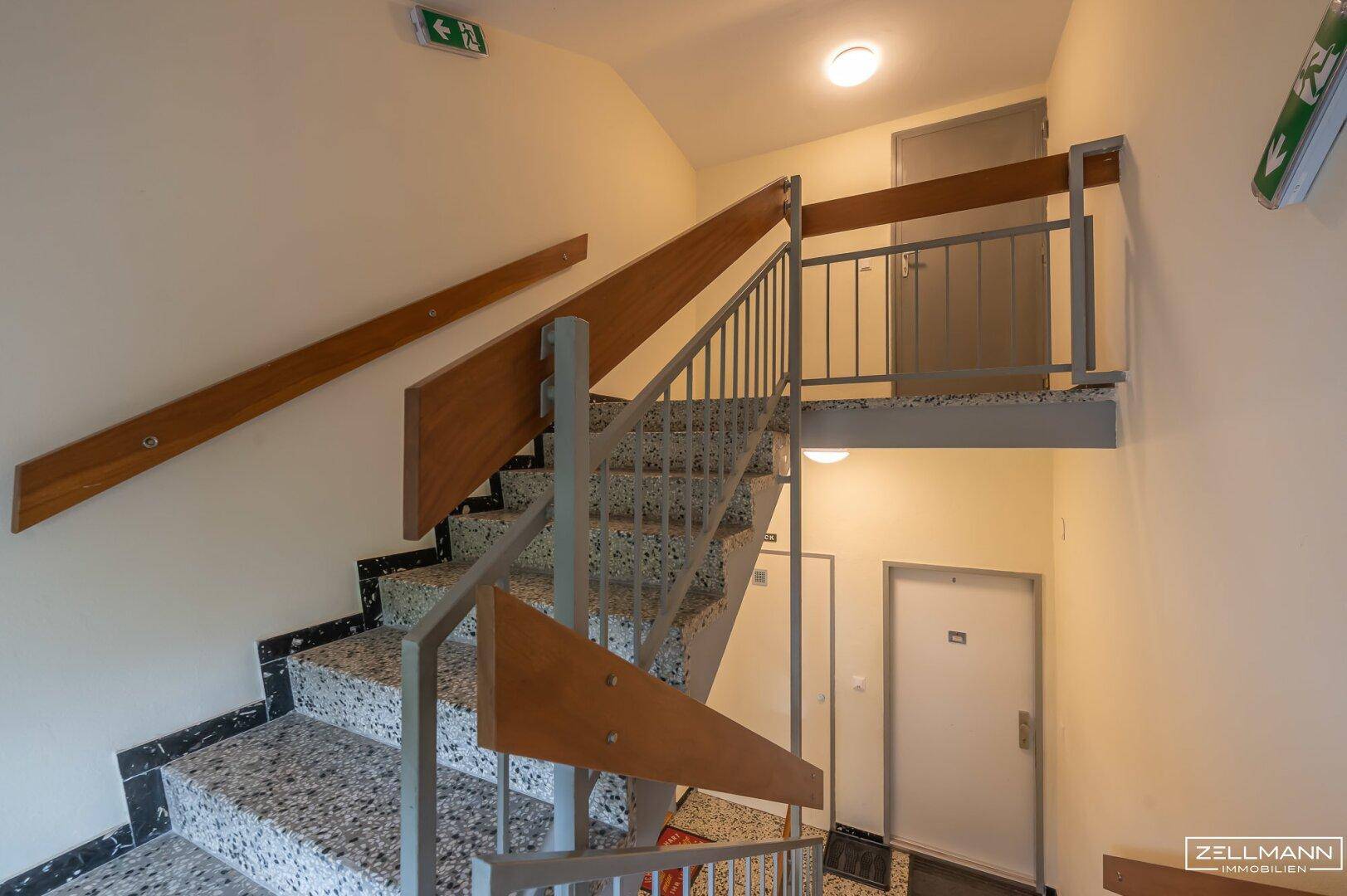 Treppenhaus mit Terrazzoboden und Holzgeländer, verbindet die Etagen des Gebäudes.