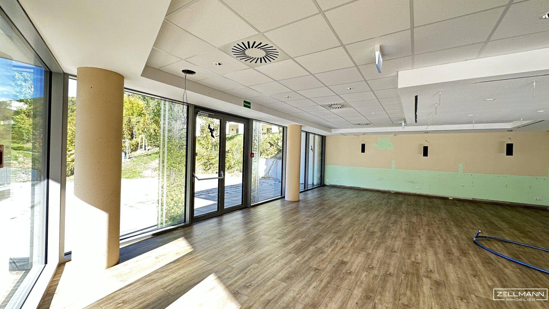 Großer, heller Gewerberaum mit durchgehenden Fensterfronten, Holzoptikboden und abgehängter Decke, renovierungsbedürftig.