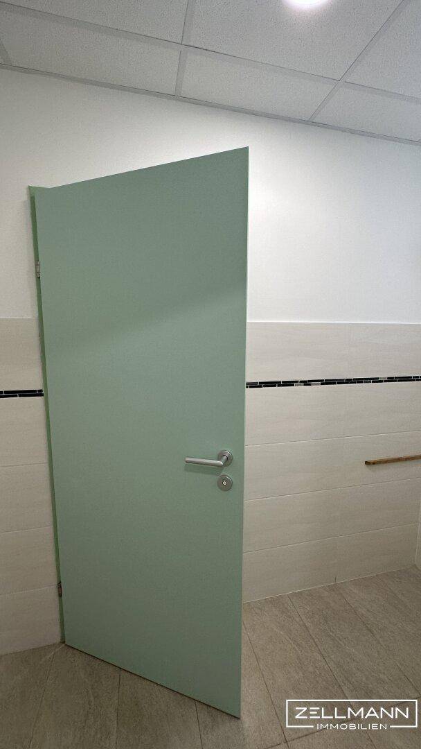 Einzelne Toilettenkabinentür in einem öffentlichen Waschraum mit hellgrüner Tür und gefliesten Wänden.
