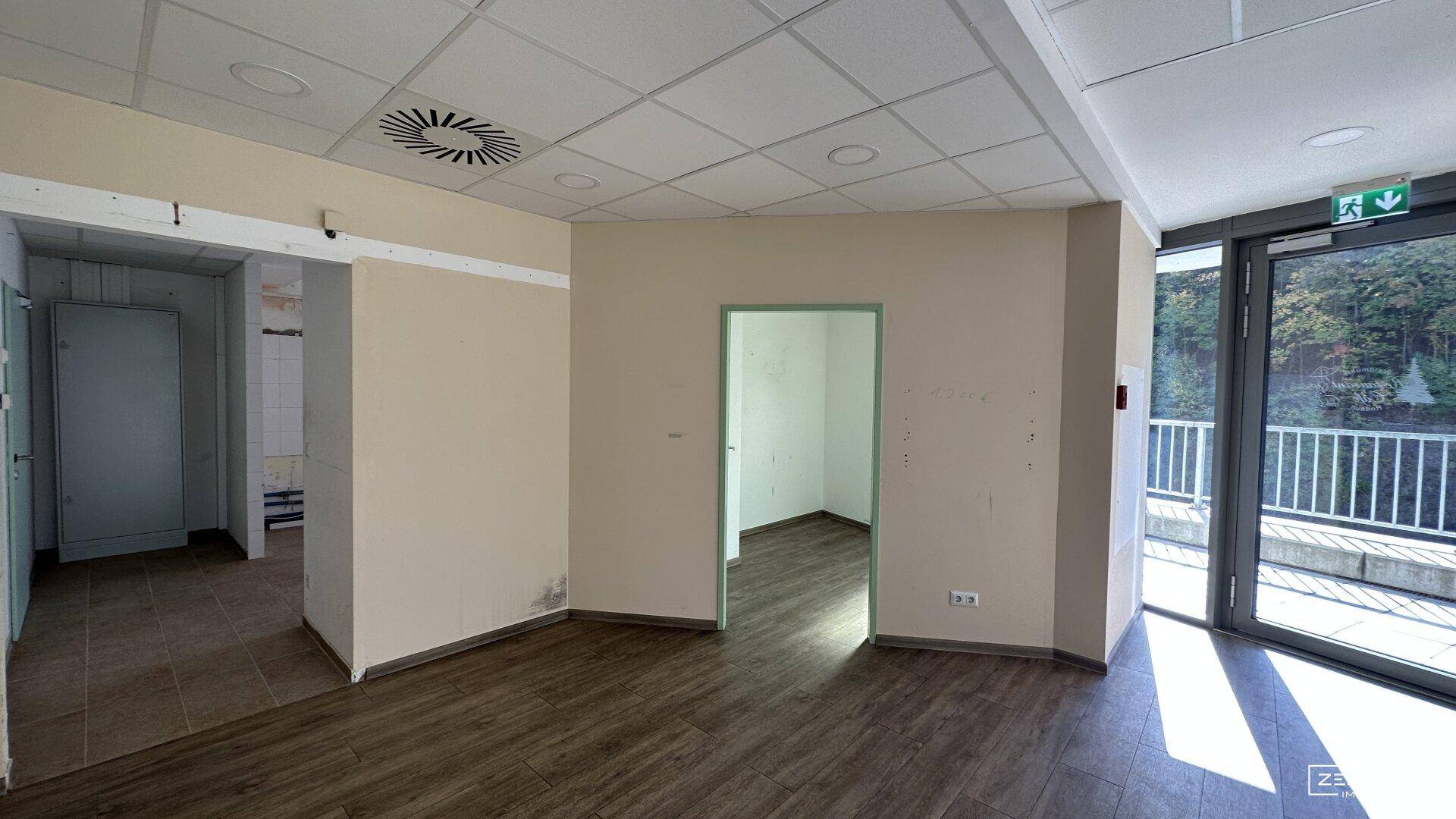 Heller Flurbereich mit Holzoptikboden, abgehängter Decke und Zugang zu weiteren Räumen sowie einem Außenausgang.
