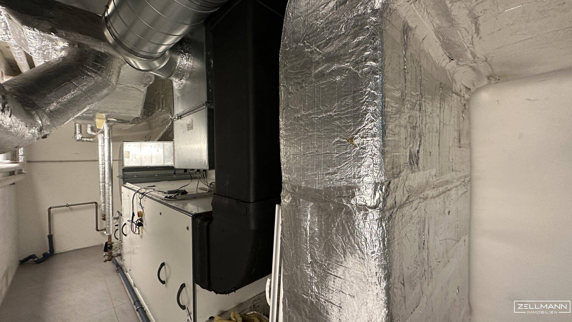Detailansicht von technischen Anlagen und isolierten Lüftungskanälen in einem Technikraum mit industriellem Charakter.