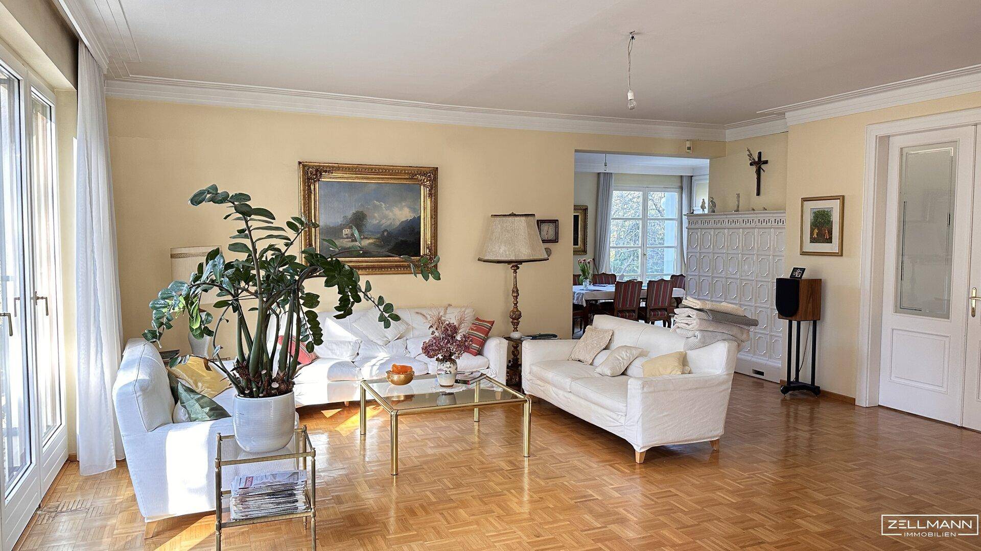 Helles Wohnzimmer mit Fischgrätparkett, gemütlichen Sofas und einem traditionellen Kachelofen.