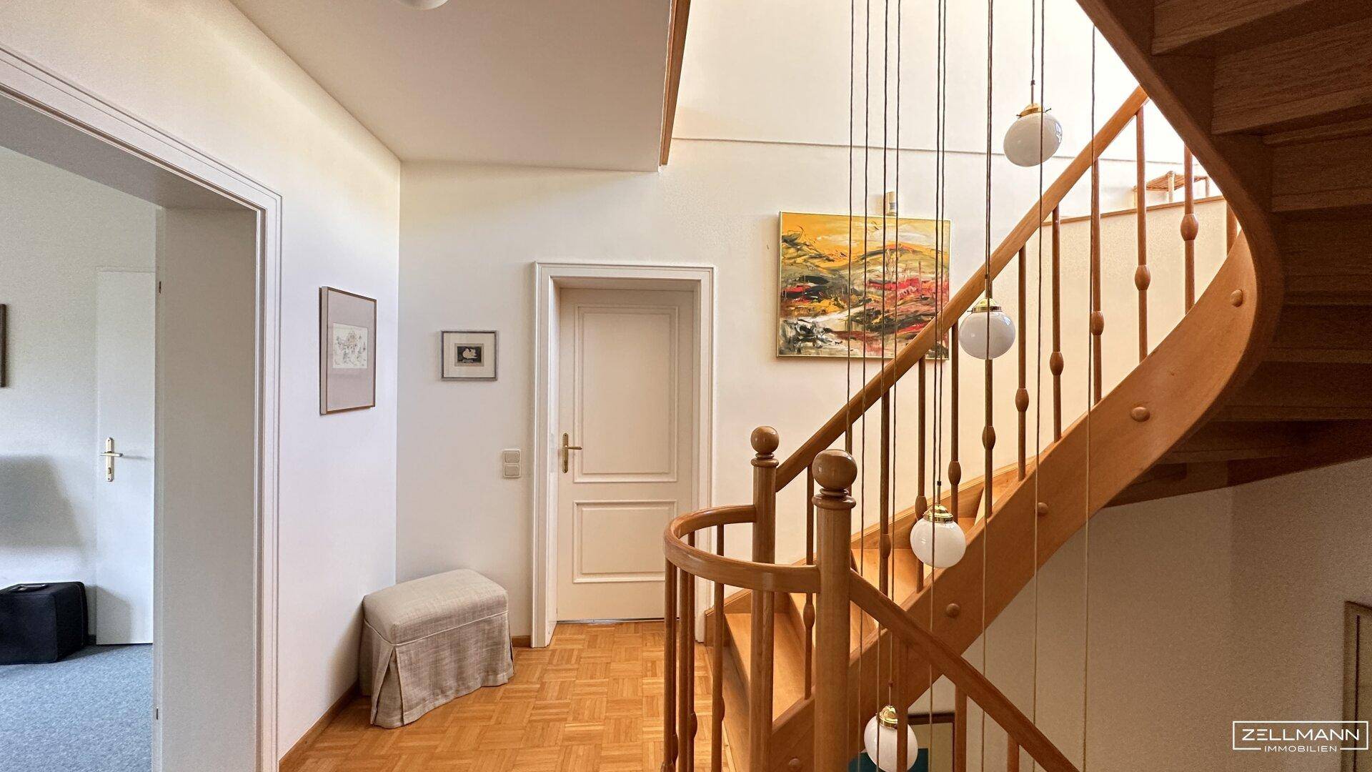 Heller Flur mit eleganter Holztreppe und Parkettboden, der zu den oberen Etagen führt.