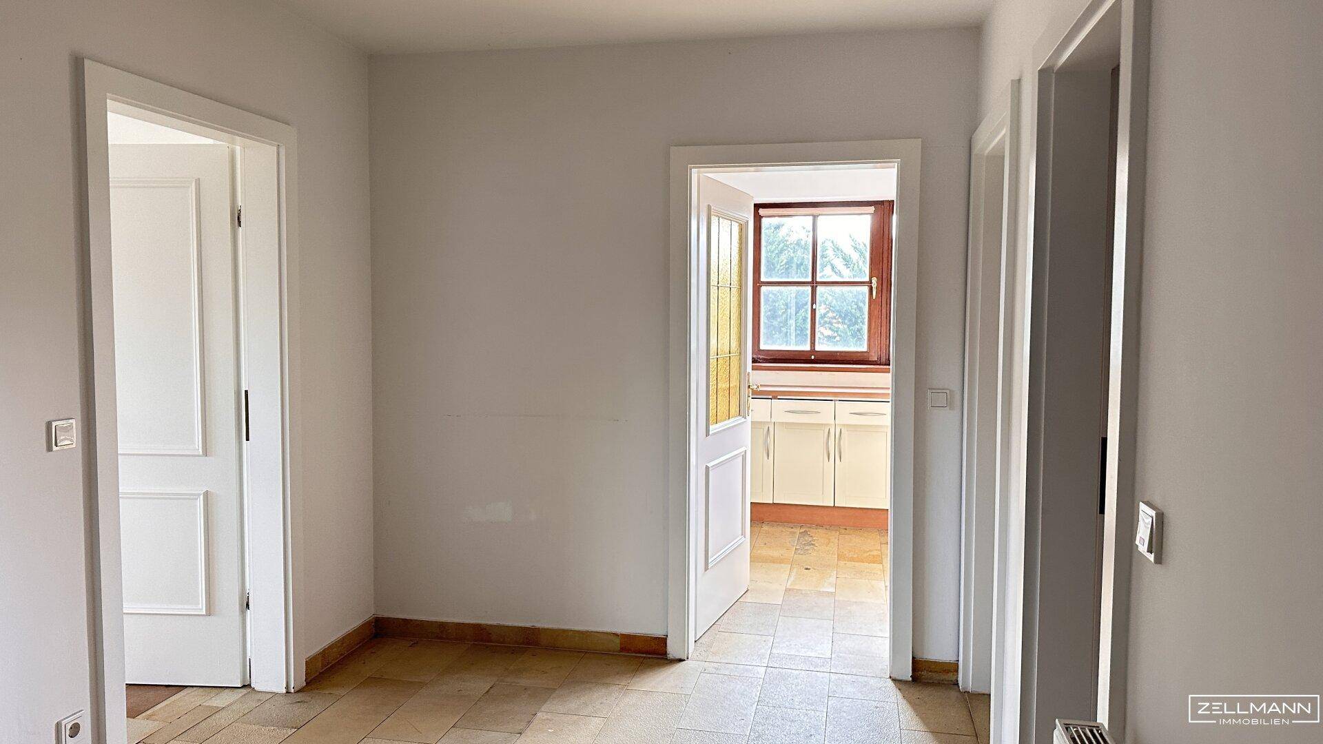 Heller Flur mit Fliesenboden und Blick durch eine Tür in eine angrenzende Küche.