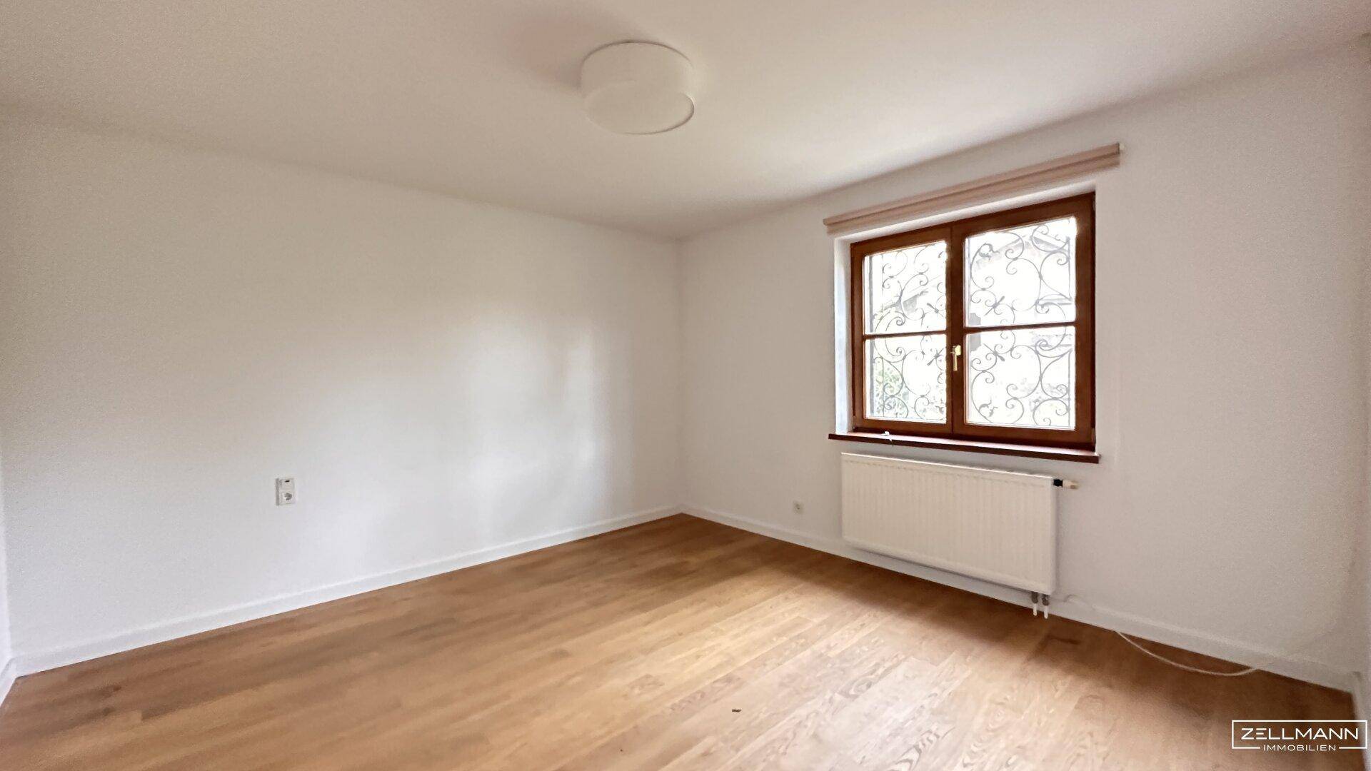 Helles Schlafzimmer mit Holzboden und einem Fenster mit Blick ins Grüne.