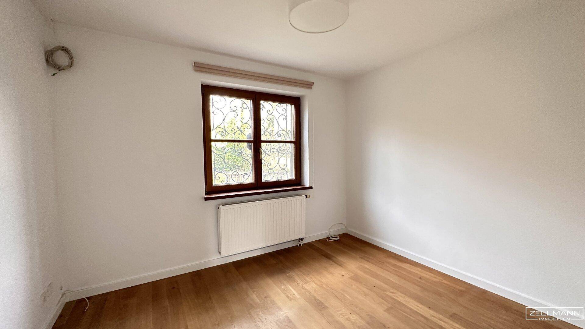 Leeres Zimmer mit Holzboden und einem Fenster, ideal als Schlaf- oder Gästezimmer.