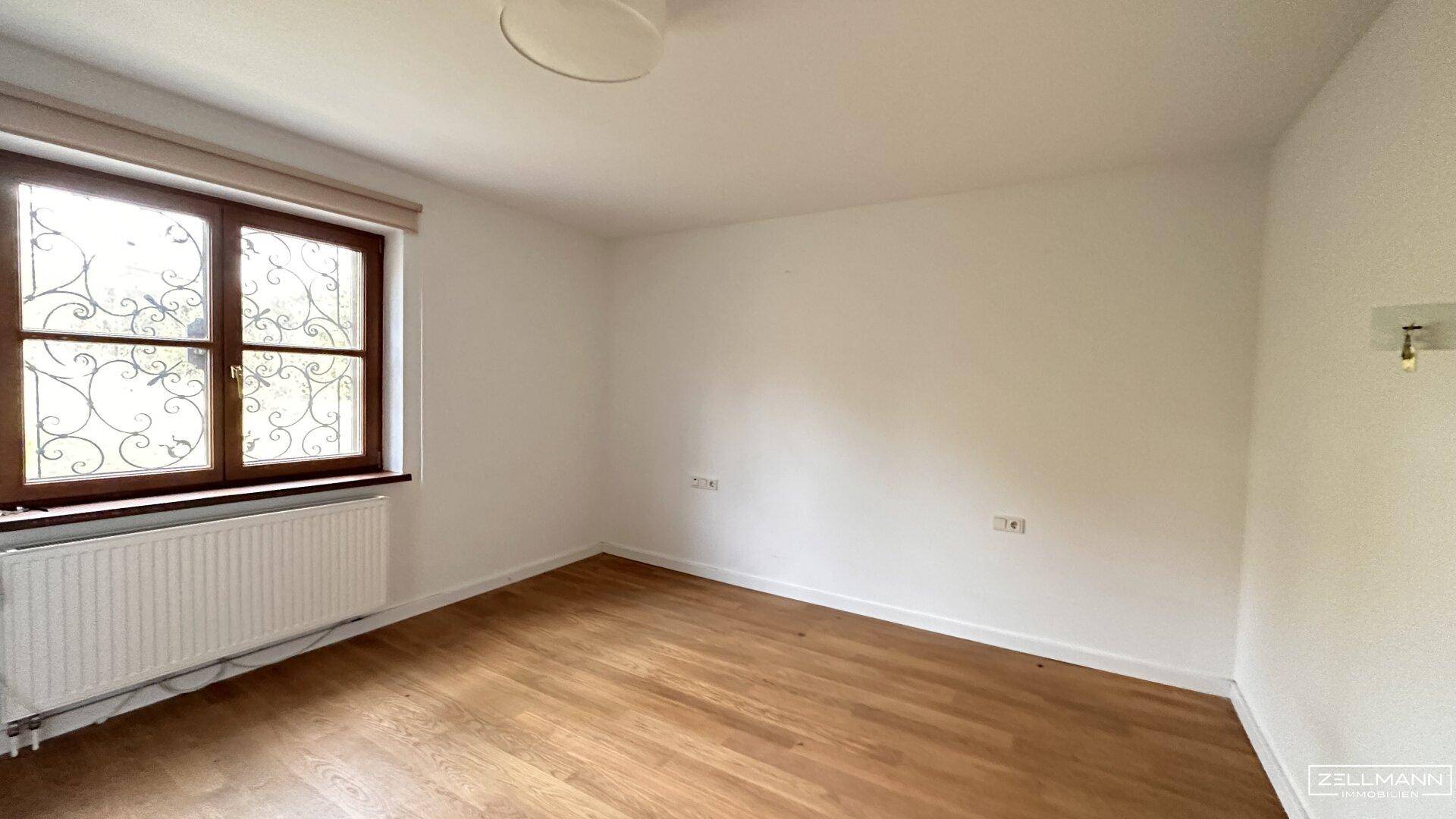 Geräumiges Zimmer mit Holzboden und Fenster, bietet vielseitige Nutzungsmöglichkeiten.