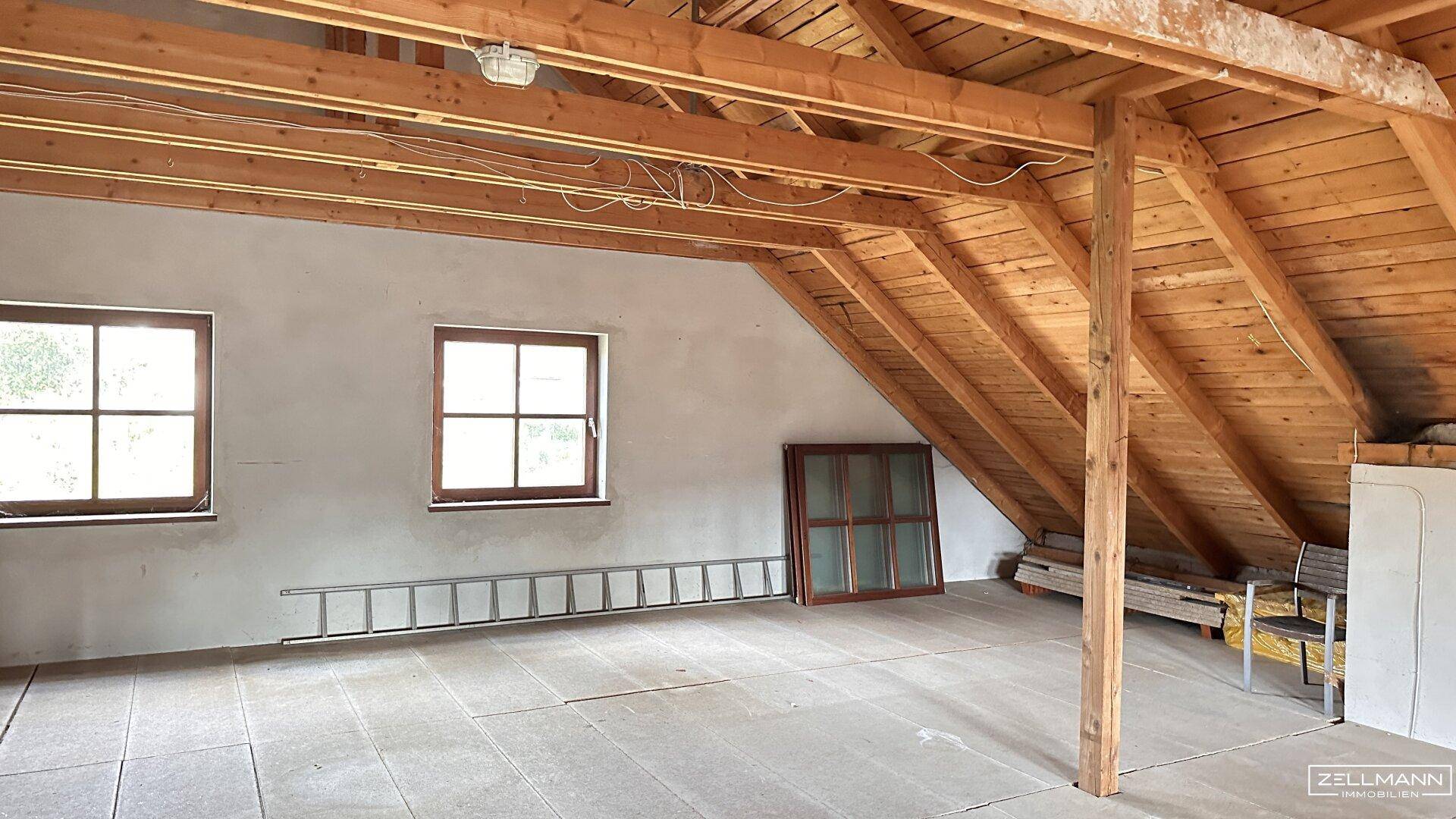 Ausbaufähiger Dachboden mit sichtbaren Holzbalken und Fenstern, bietet viel Potenzial.