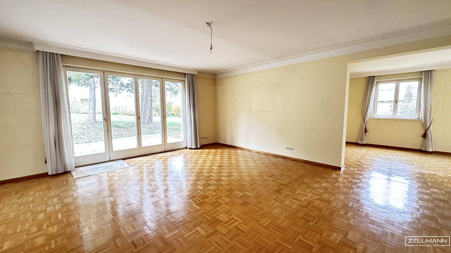 Geräumiger, leerer Raum mit Parkettboden und großen Glastüren zum Garten.