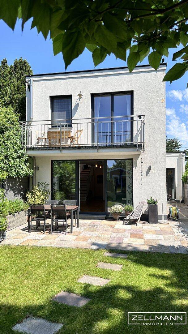 Moderne Hausfassade mit Balkon und Terrasse, umgeben von üppigem Grün.