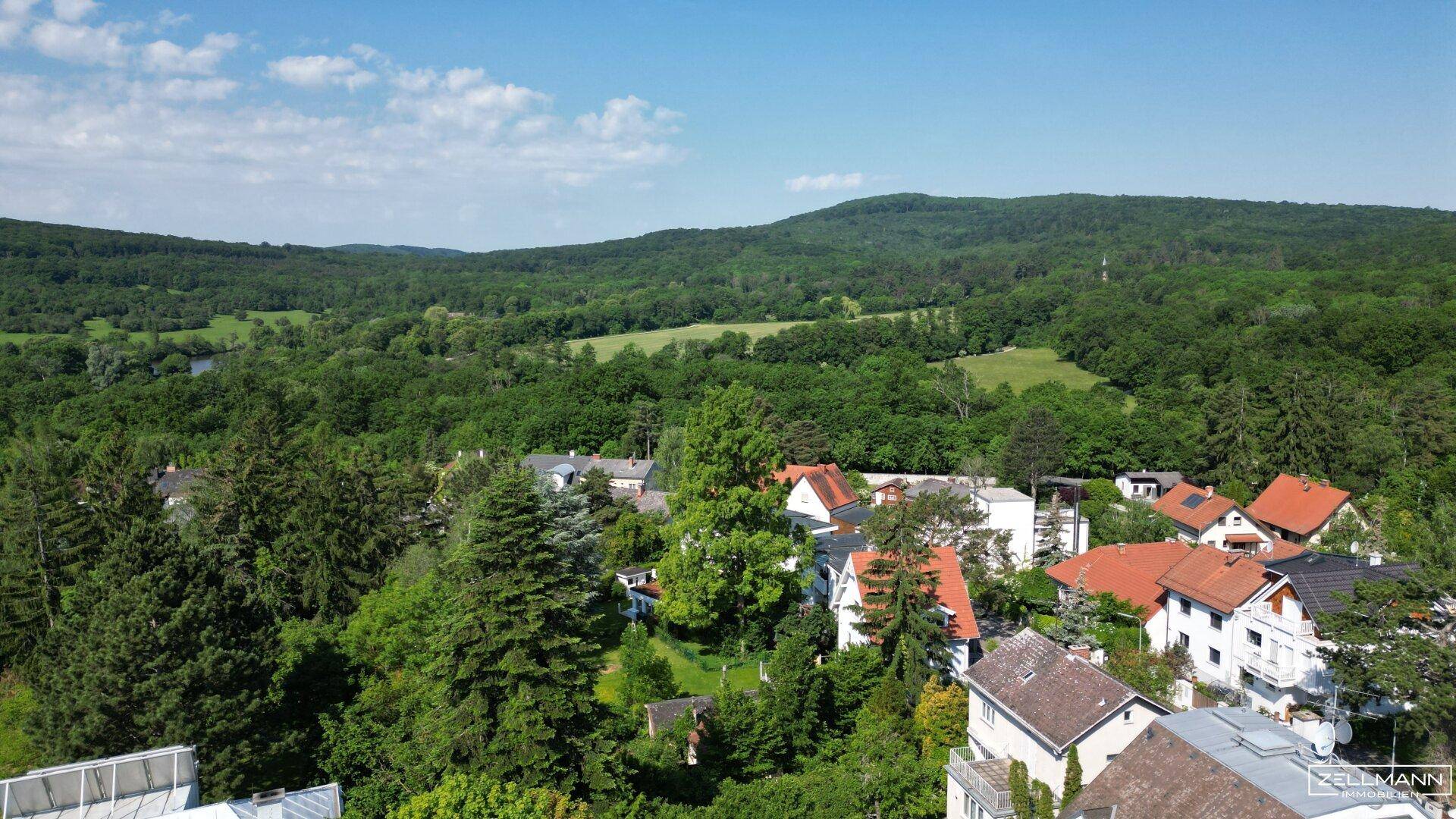 Panoramablick über eine grüne Wohnsiedlung mit weitem Horizont und bewaldeten Hügeln.