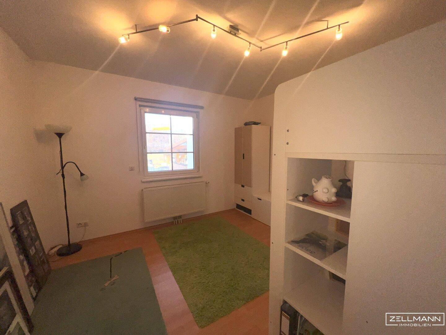 Helles Kinderzimmer mit Fenster, Teppich und Stauraum, bietet eine freundliche Lernumgebung.