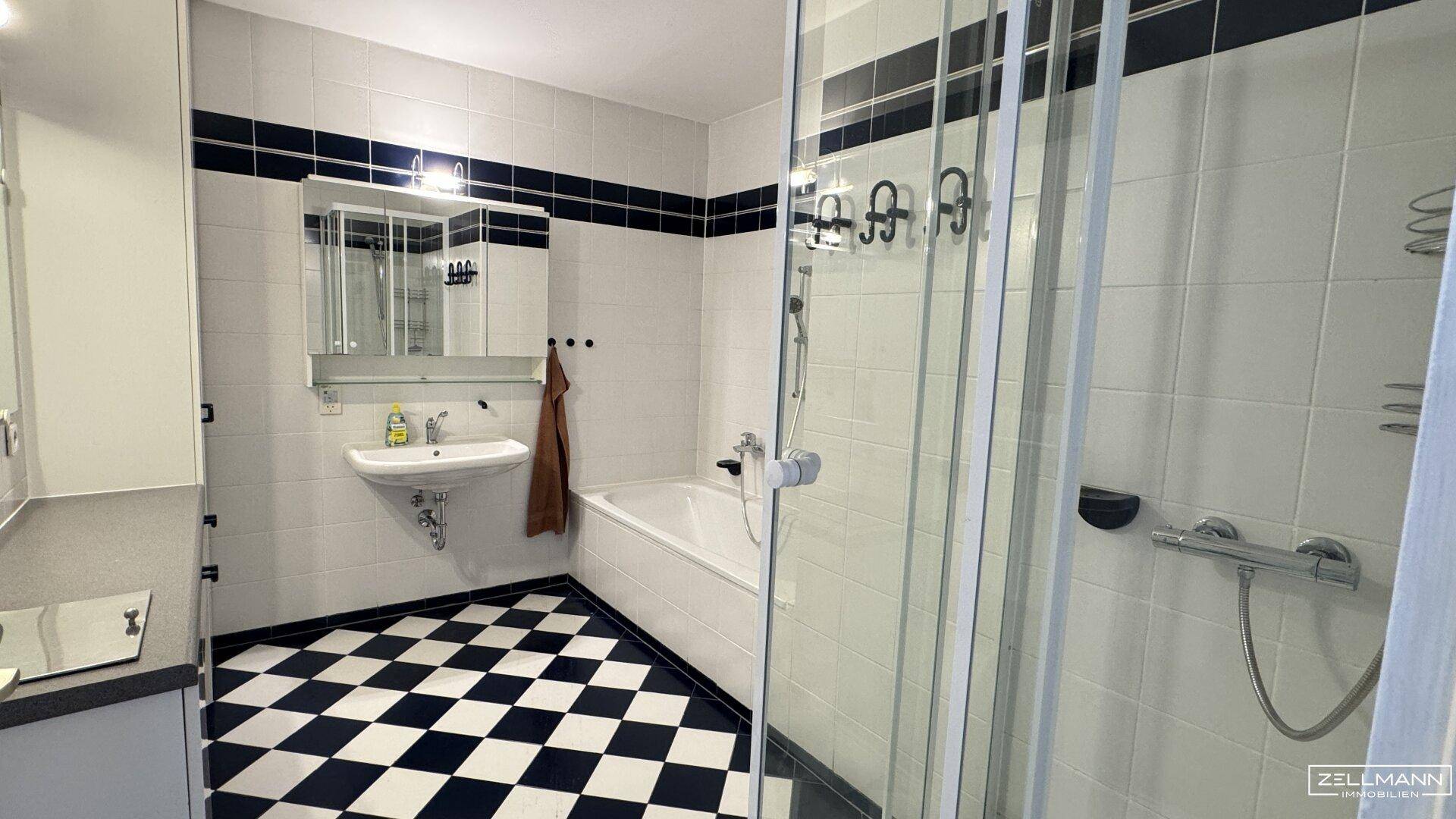 Badezimmer mit weiß-blauen Fliesen, kariertem Boden, Badewanne, Duschkabine und Spiegelschrank.