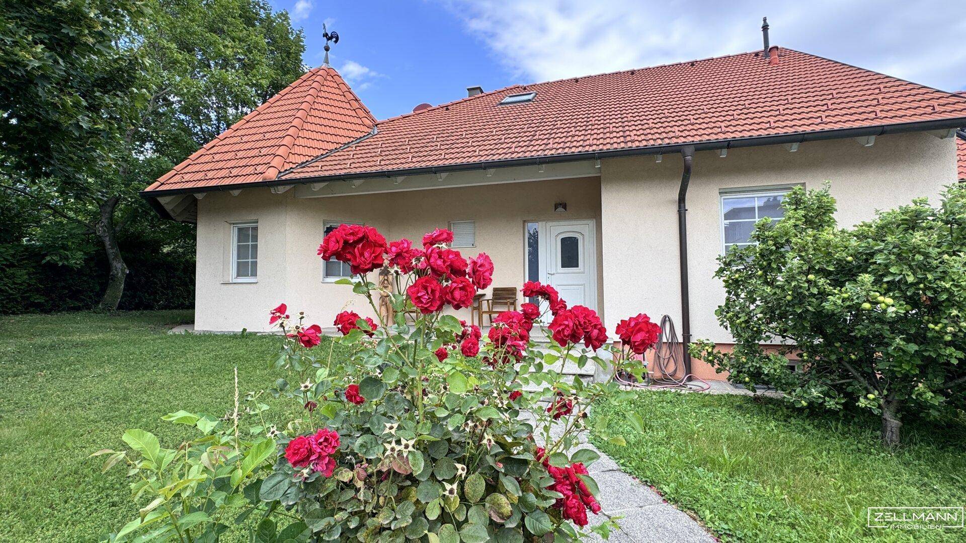Vorderansicht des Hauses mit blühenden Rosen und gepflegtem Vorgarten unter blauem Himmel.