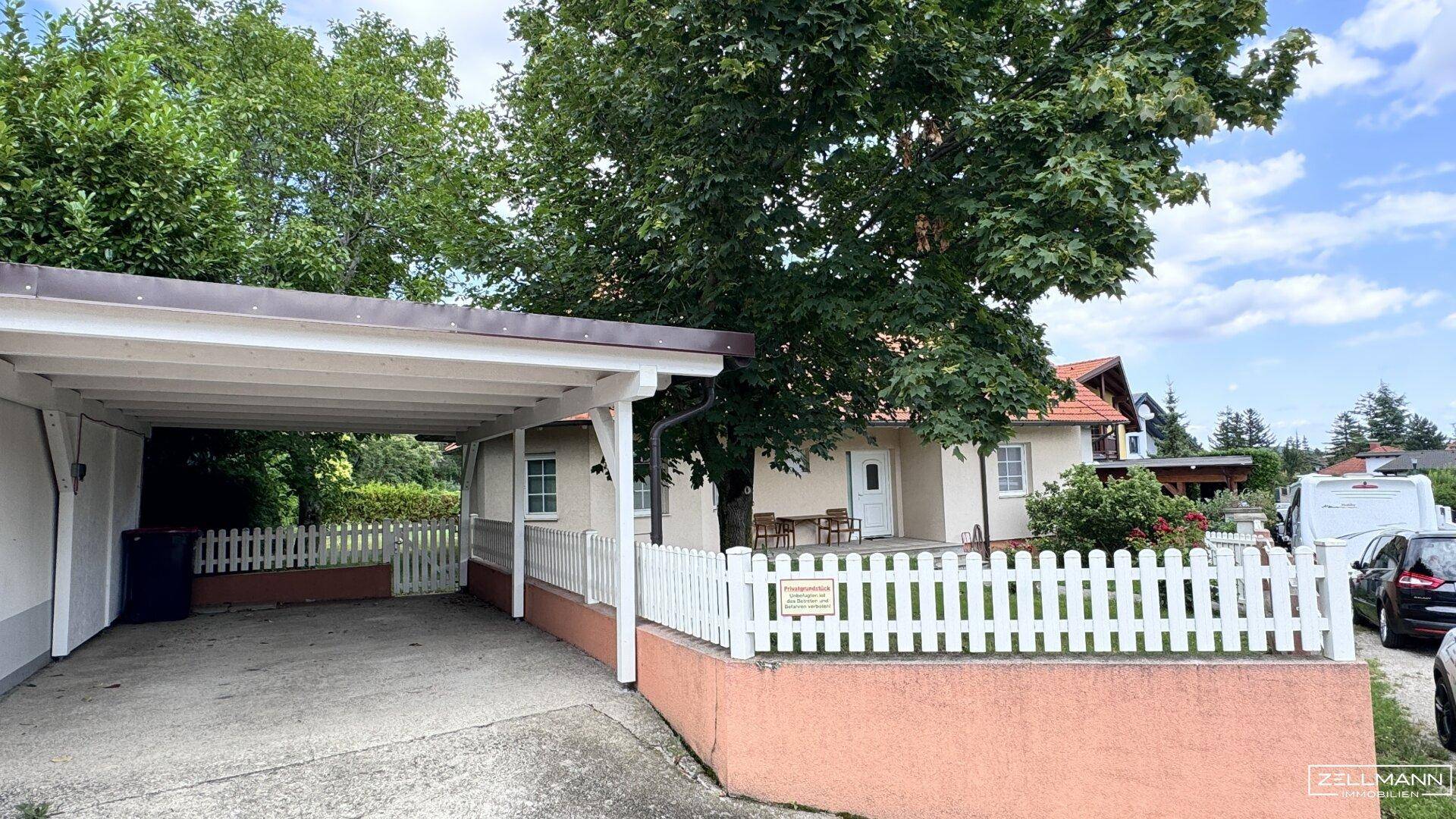 Carport und Zufahrt zum Haus mit weißem Zaun, bietet bequemen Zugang und Parkmöglichkeiten.