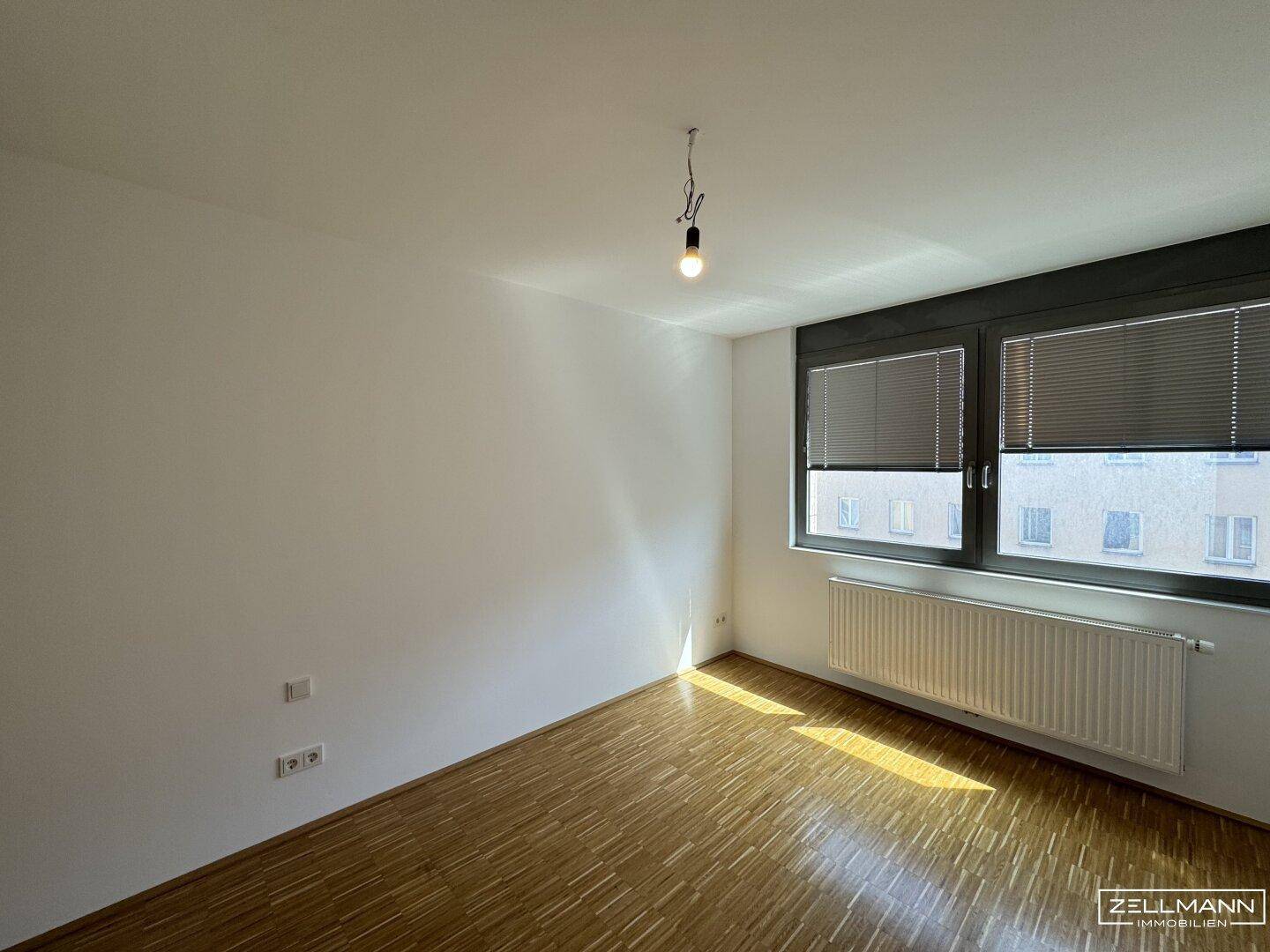 Geräumiger, heller Raum mit Laminatboden und Fensterfront, bietet viel Tageslicht.