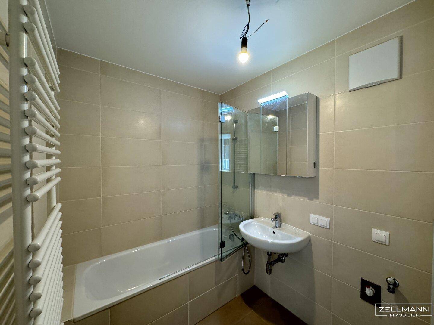 Modernes Badezimmer mit beigefarbenen Fliesen, Badewanne und Waschbecken mit Spiegelschrank.