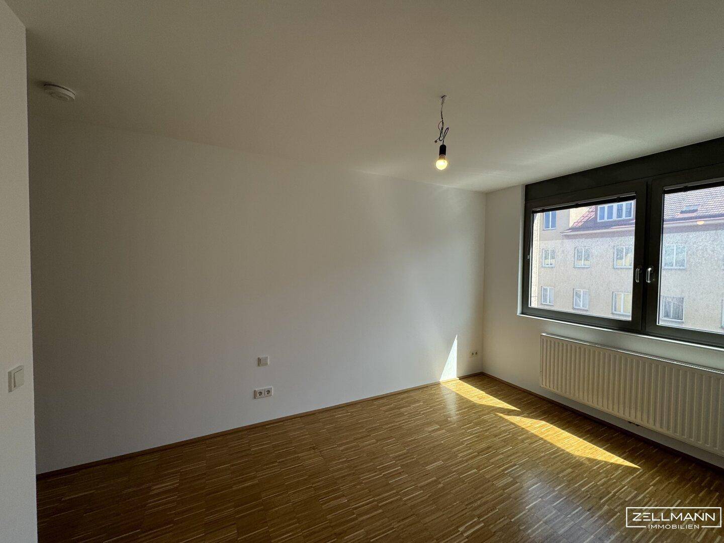 Heller Raum mit Laminatboden, großen Fenstern und Heizkörper, bereit zur Einrichtung.