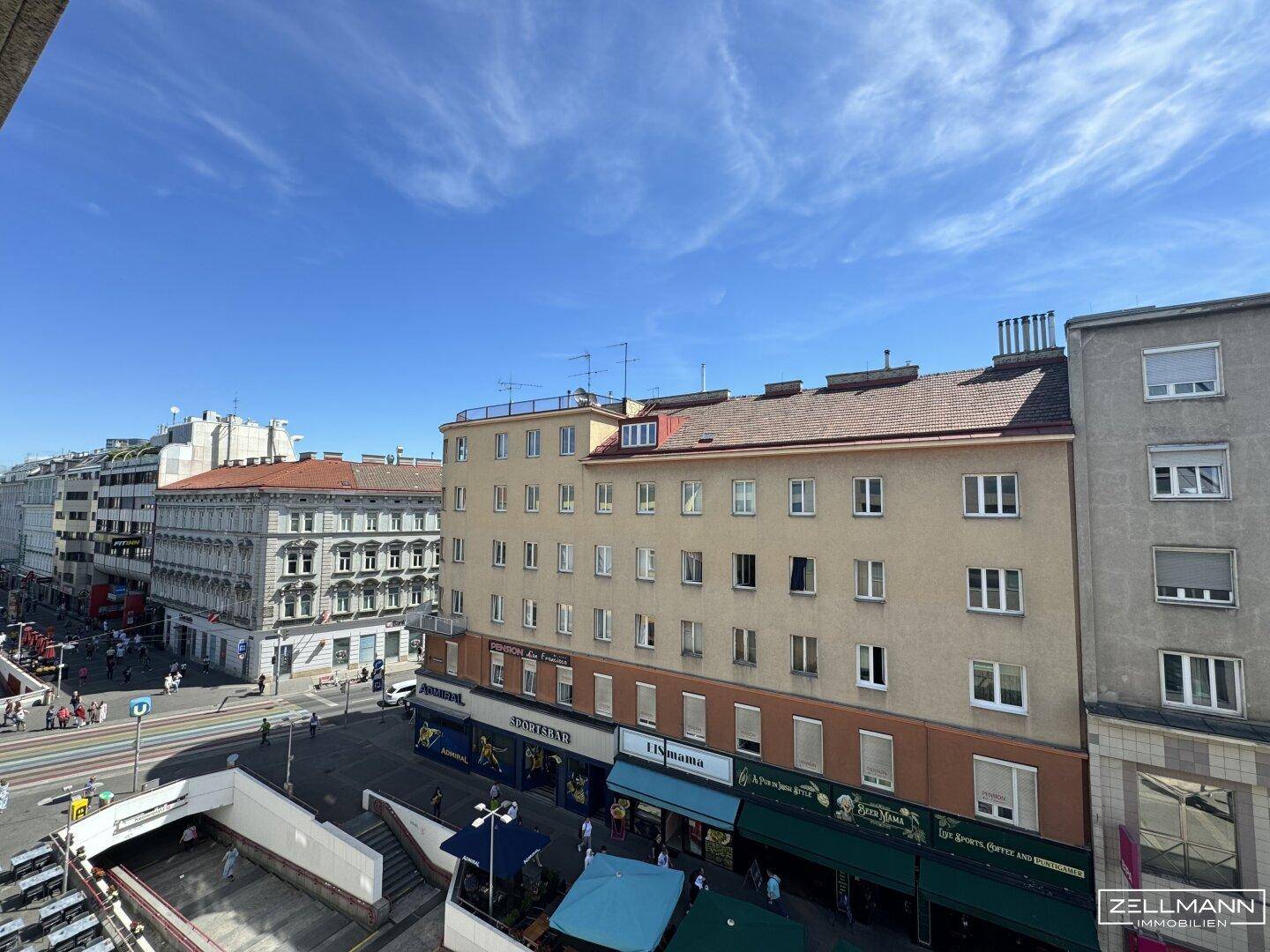 Weitläufiger Blick über eine belebte Stadtstraße mit Gebäuden und blauem Himmel.