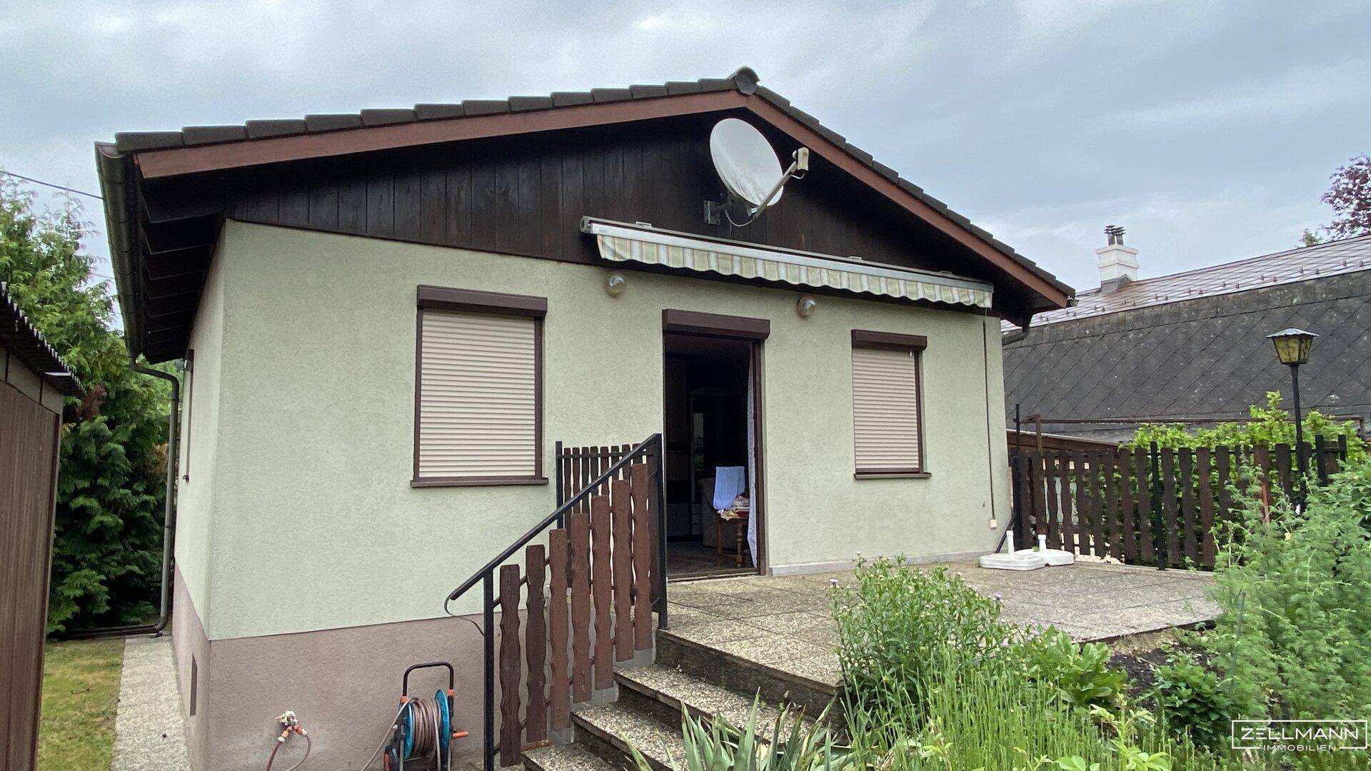 Rückseite des Hauses mit kleiner gepflasterter Terrasse, Außentreppe und Satellitenschüssel.