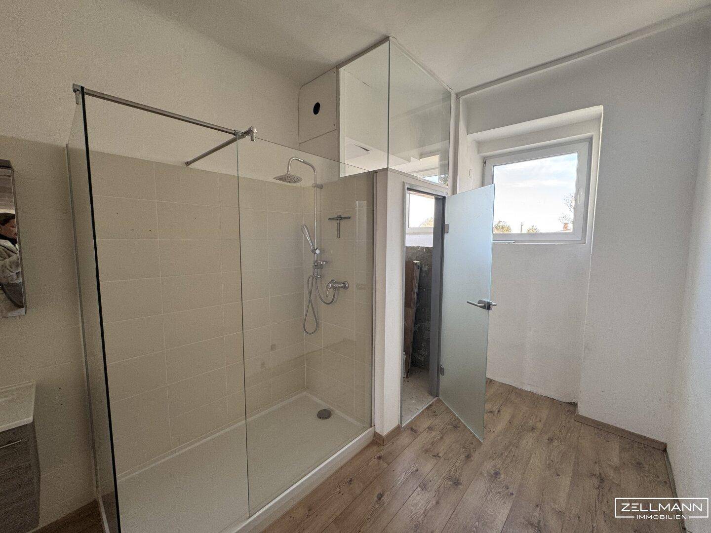Modernes Badezimmer mit einer begehbaren Glasdusche und einem Fenster für Tageslicht.