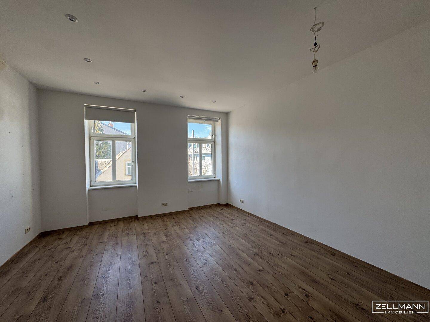 Heller, leerer Raum mit Holzdielenboden und zwei großen Fenstern.