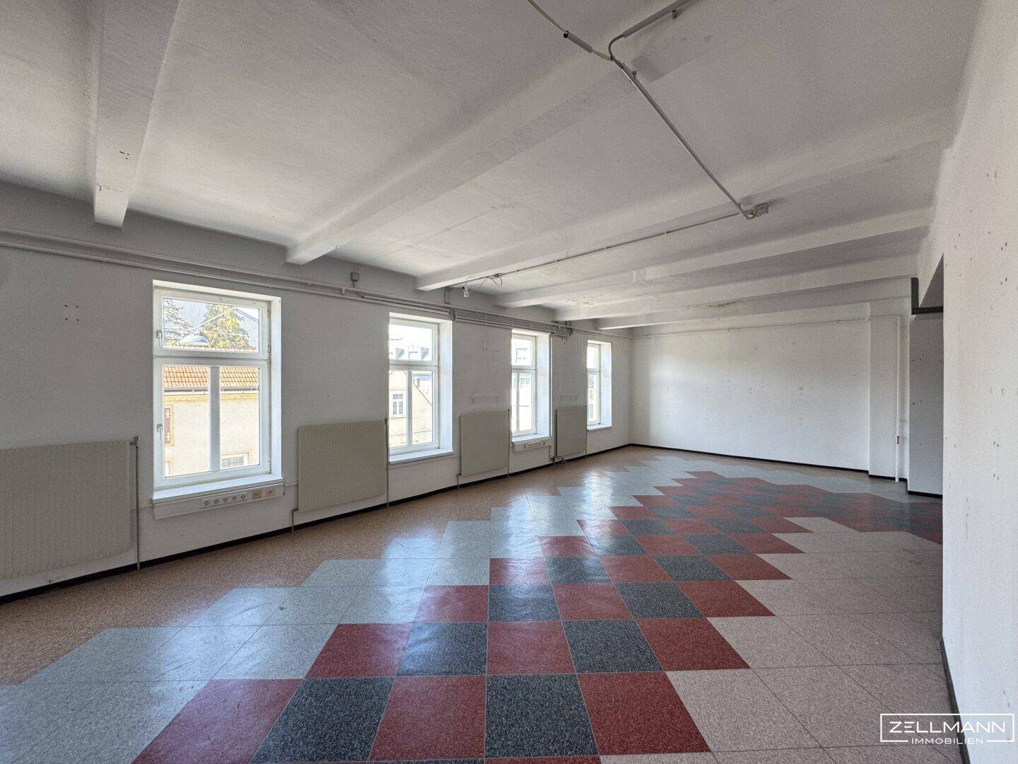 Heller, weitläufiger Innenraum mit einem markanten Fliesenboden und sichtbaren Deckenbalken, ideal für verschiedene Nutzungen.