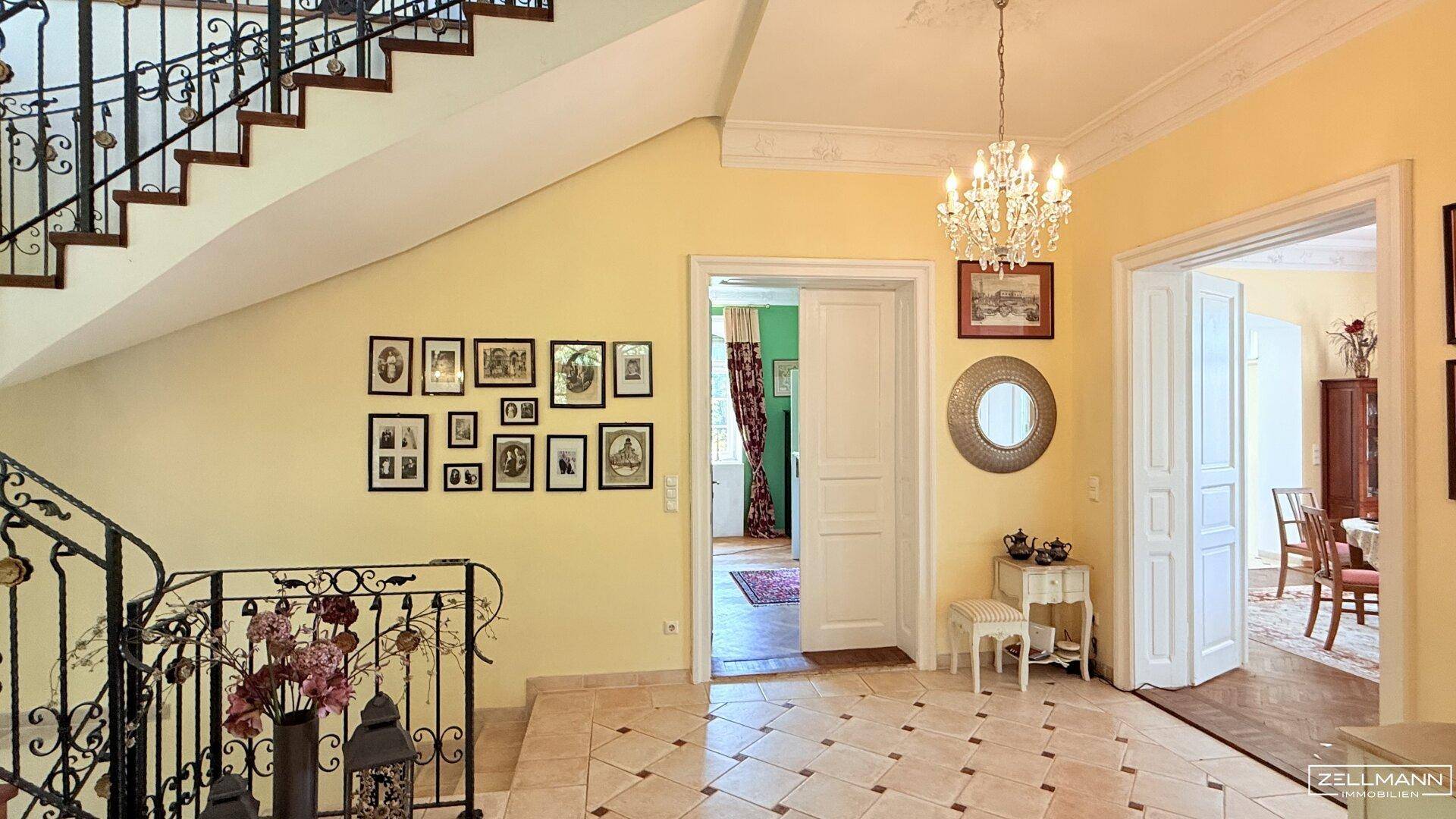 Elegante Eingangshalle mit geschwungener Treppe, Stuckdecke und Fliesenboden.