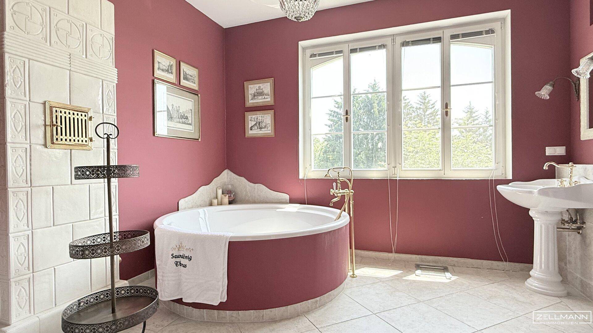 Geräumiges Badezimmer mit runder Badewanne, Kachelofen und Fenster zum Garten.