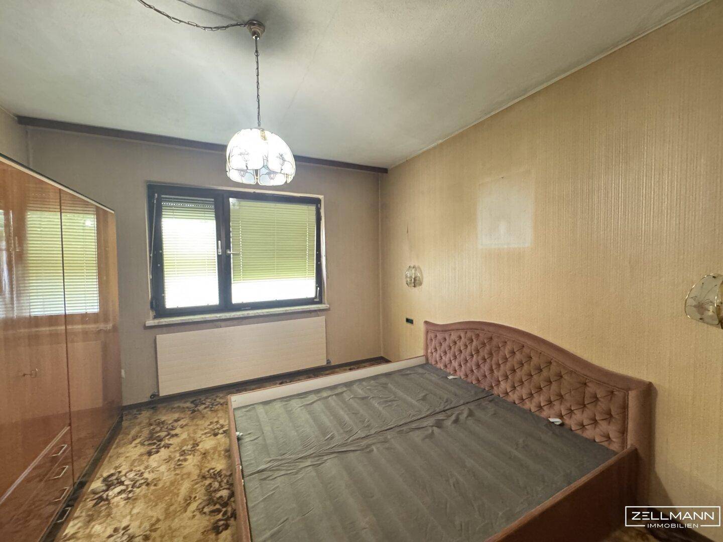 Schlafzimmer mit Teppichboden, Fenster und einem Bett mit gepolstertem Kopfteil in traditionellem Stil.