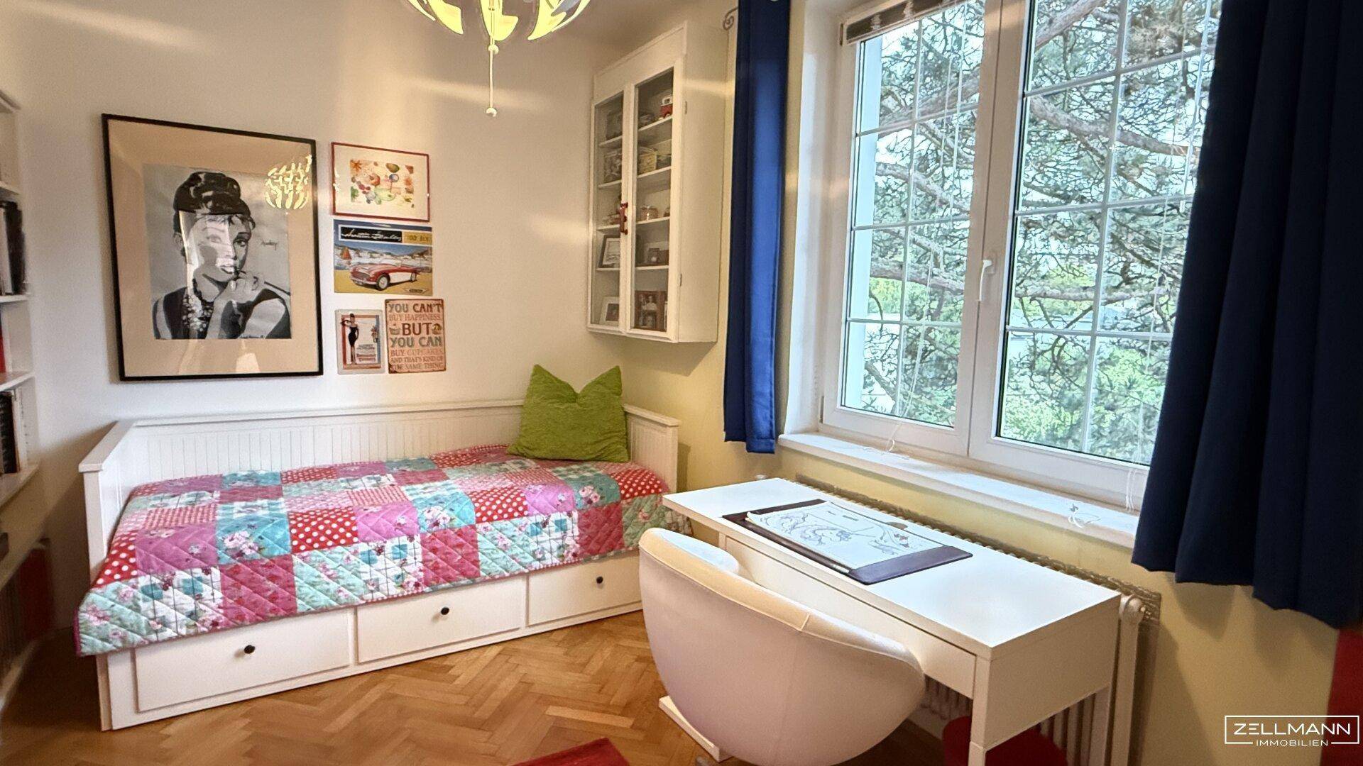 Helles Schlafzimmer mit Einzelbett, Schreibtisch und großem Fenster mit Blick ins Grüne.