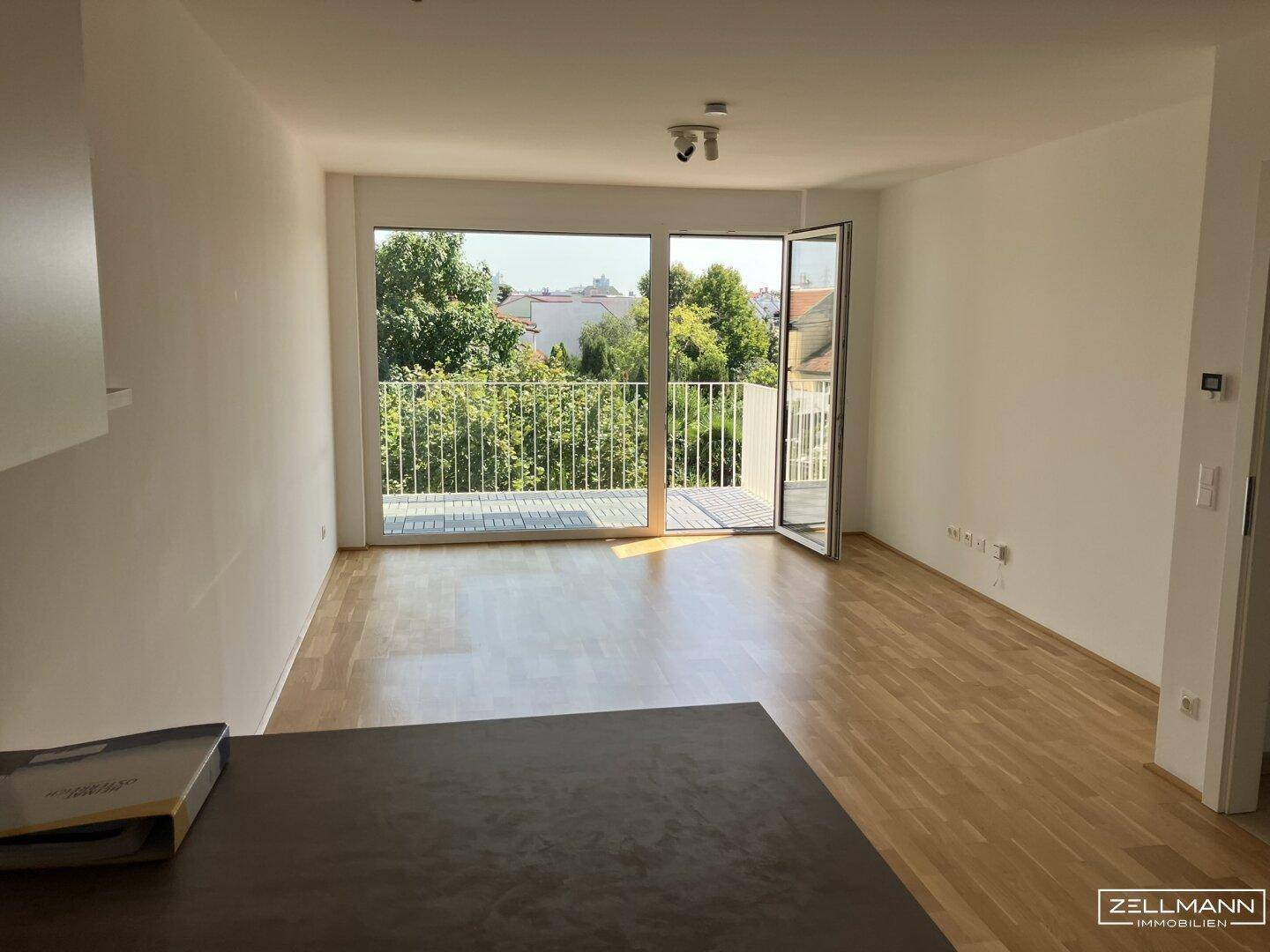 Helles Wohnzimmer mit Holzboden und Zugang zu einem Balkon mit grüner Aussicht.