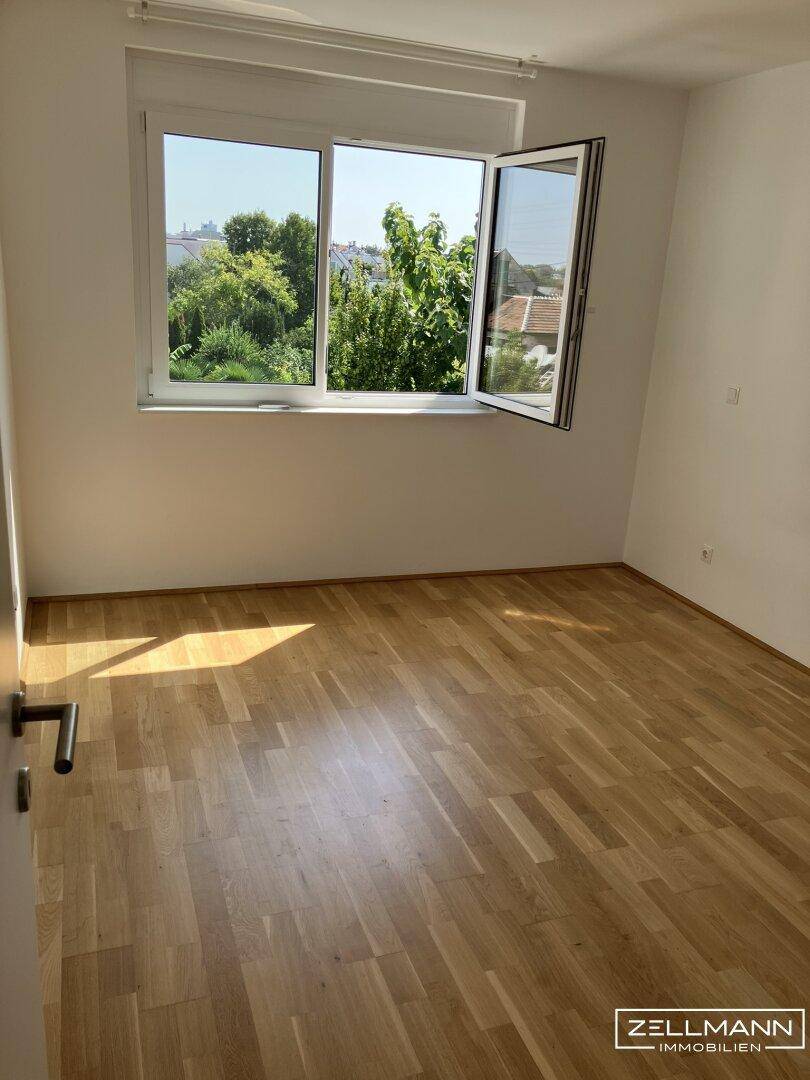 Helles Schlafzimmer mit Holzboden und großem Fenster mit Blick ins Grüne.