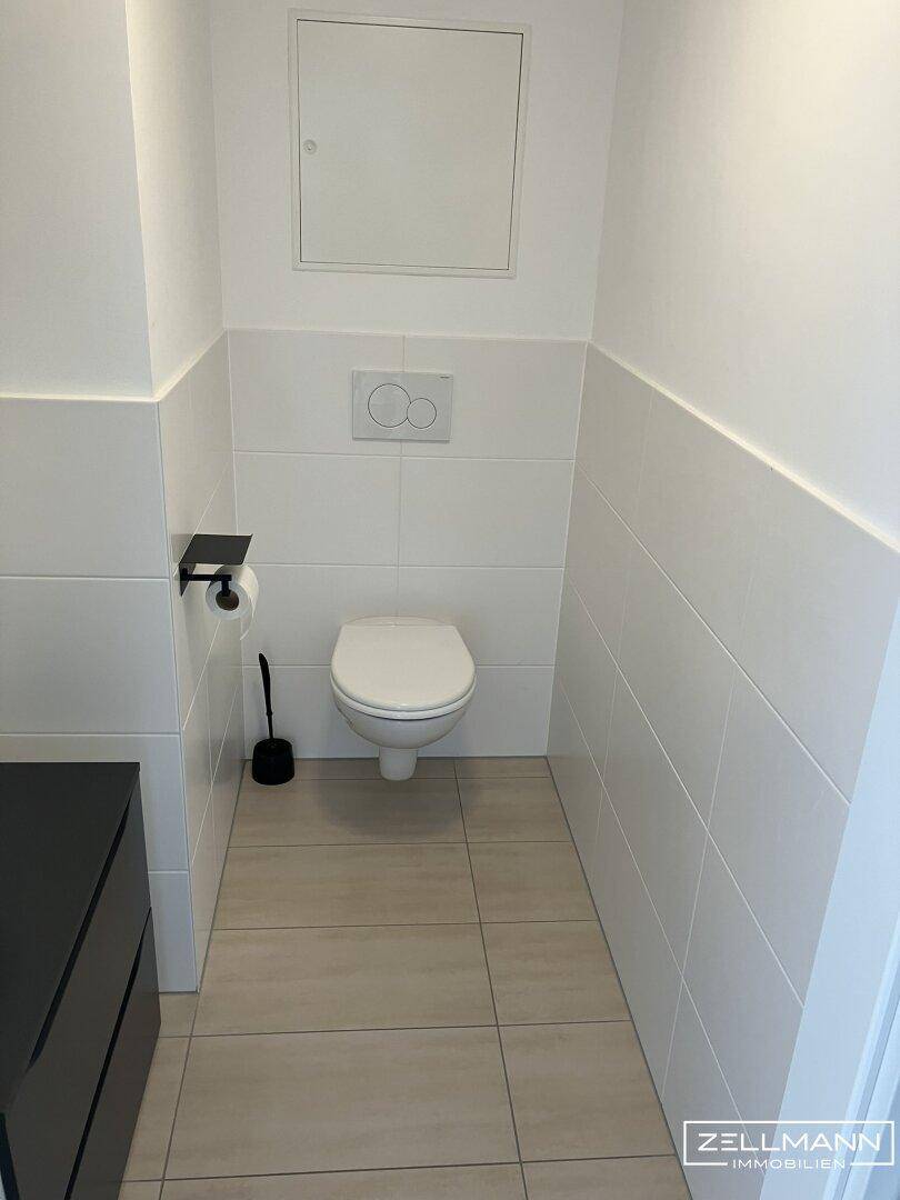 Separates WC mit wandhängender Toilette und modernen Fliesen an Boden und Wänden.
