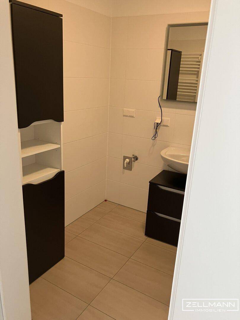 Badezimmer mit Waschbecken, Spiegelschrank und hohem Stauraumschrank auf Fliesenboden.