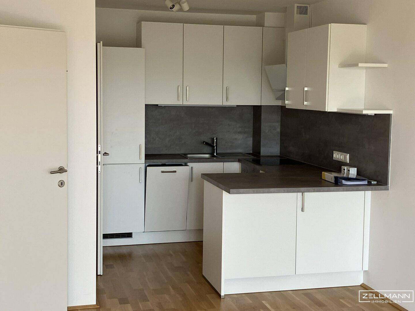 Moderne Einbauküche mit weißen Schränken, dunkler Arbeitsplatte und Holzboden.