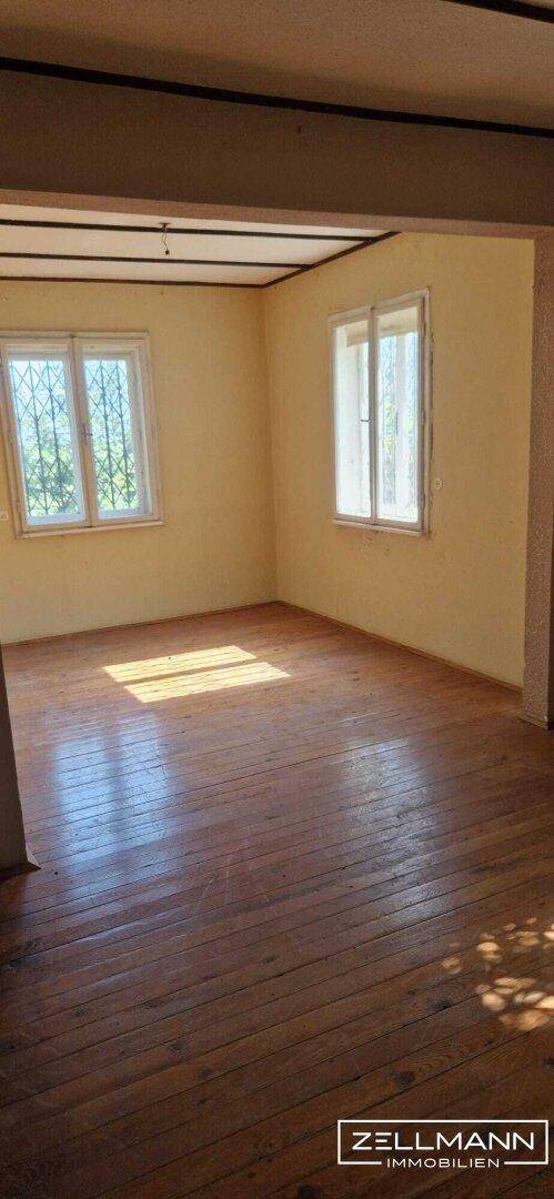 Helles, leeres Zimmer mit Holzdielenboden und hellgelben Wänden, durchflutet von natürlichem Sonnenlicht.